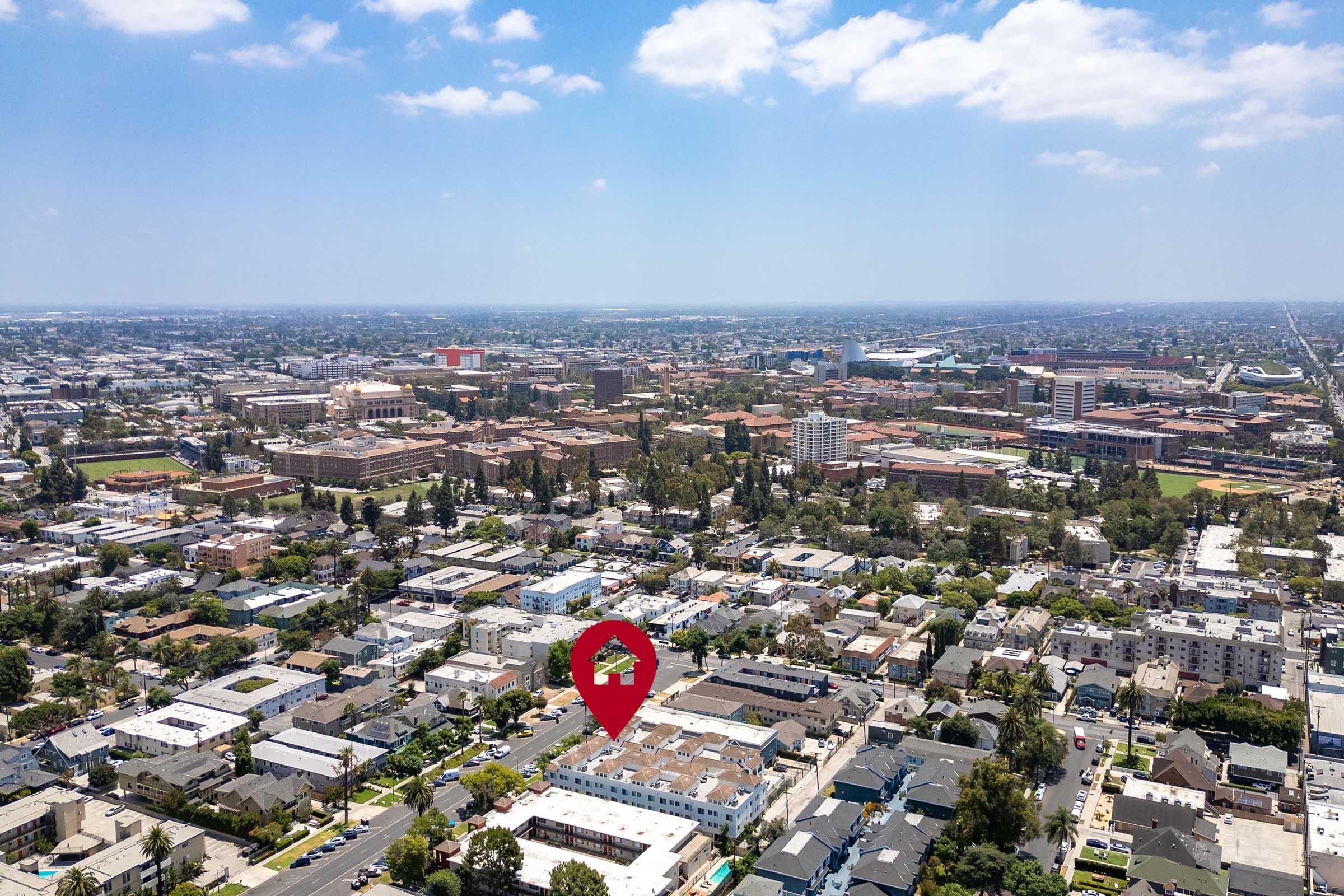 Aerial view of a cityscape showcasing a densely populated urban area with various buildings, streets, and greenery. A red marker indicates a specific location amidst the expansive view, featuring low-rise structures and a mix of residential and commercial properties in the vicinity.