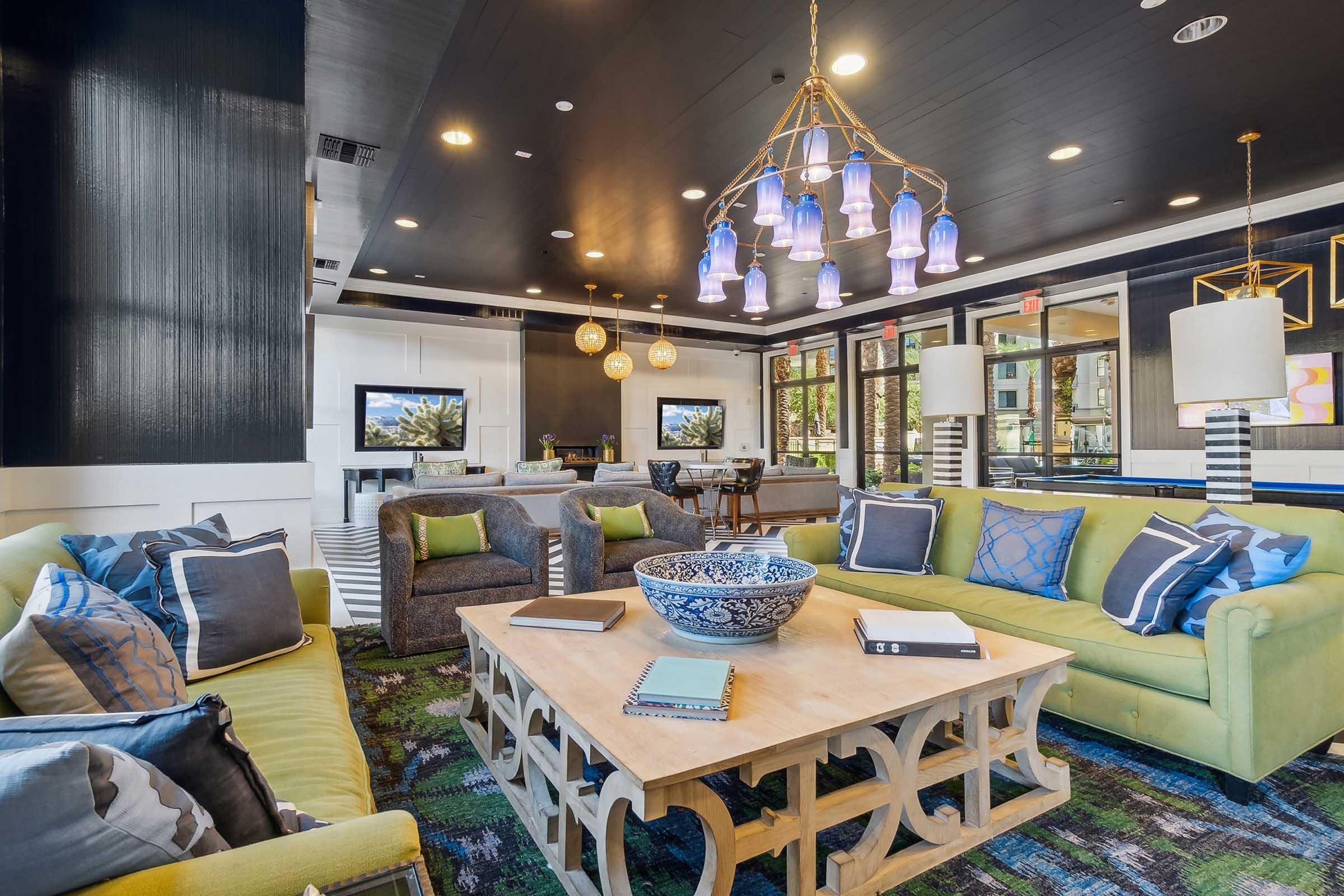 A modern, stylish lounge area featuring a bright green sofa with blue and gray cushions, a rustic wooden coffee table, and a colorful decorative bowl.