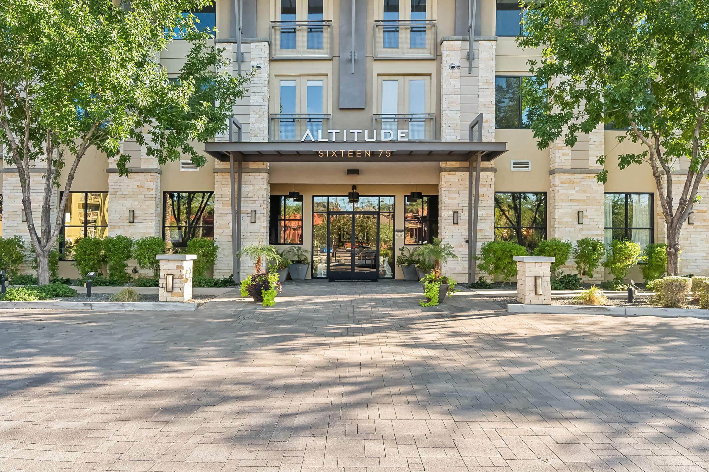 Exterior view of the Altitude Sixteen 75 apartment building, featuring modern architecture, large glass entrance doors, and surrounding landscaping with trees and plants.