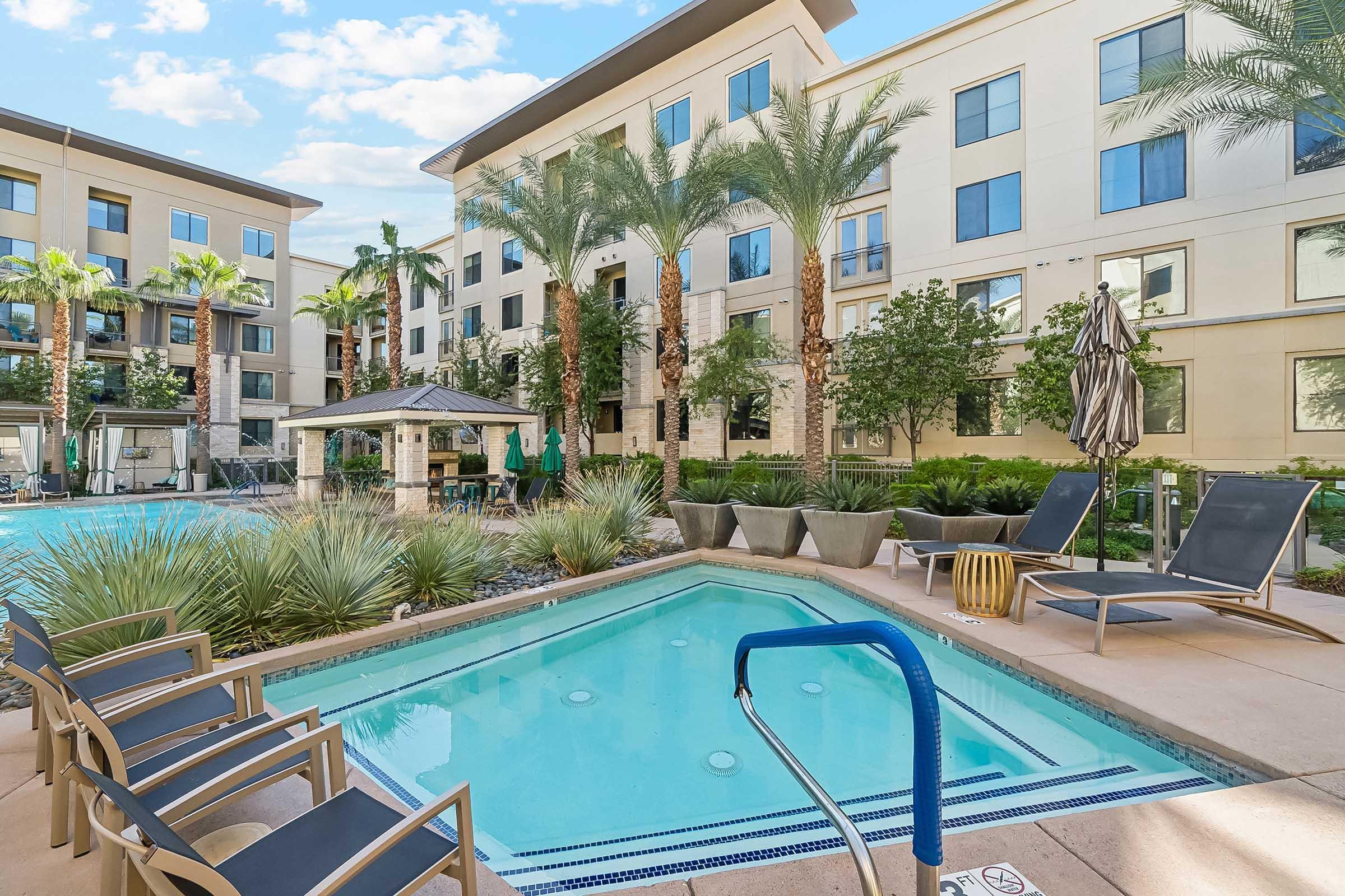 A serene outdoor pool area featuring a clear blue pool, tropical palm trees, and comfortable lounge chairs.