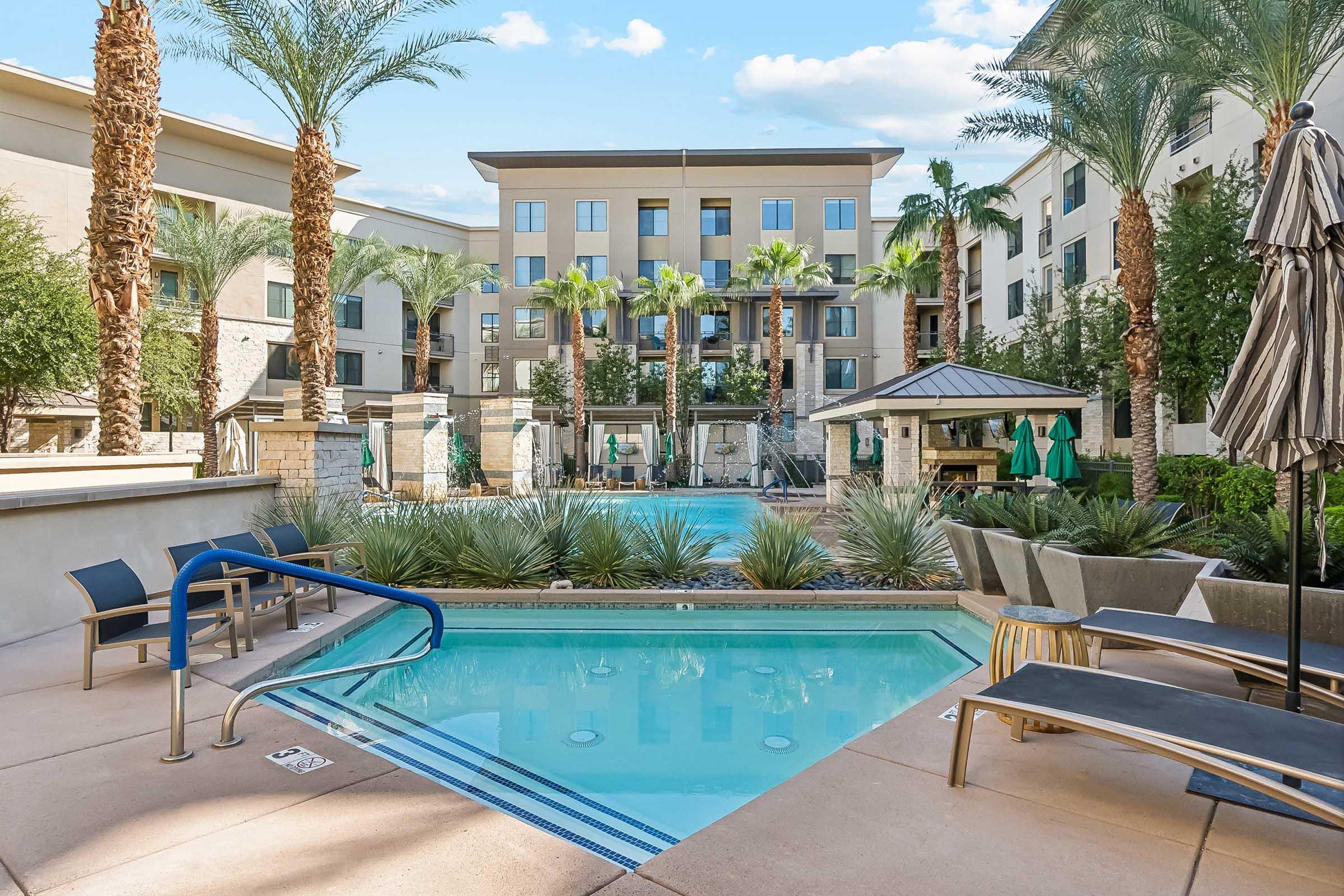 A serene pool area featuring a clear blue pool surrounded by palm trees and lush greenery.