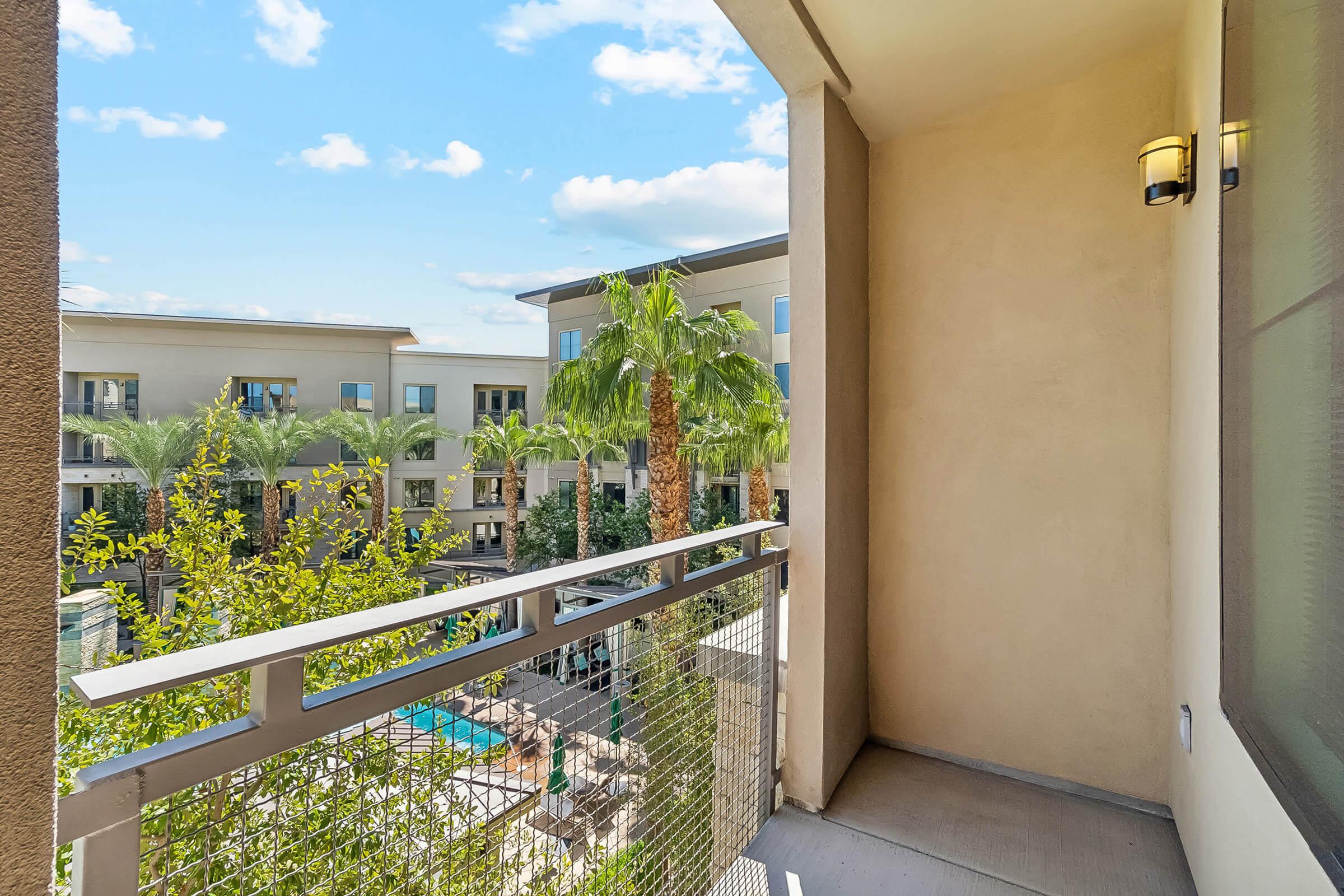 View from a balcony overlooking a landscaped courtyard with palm trees and a swimming pool.