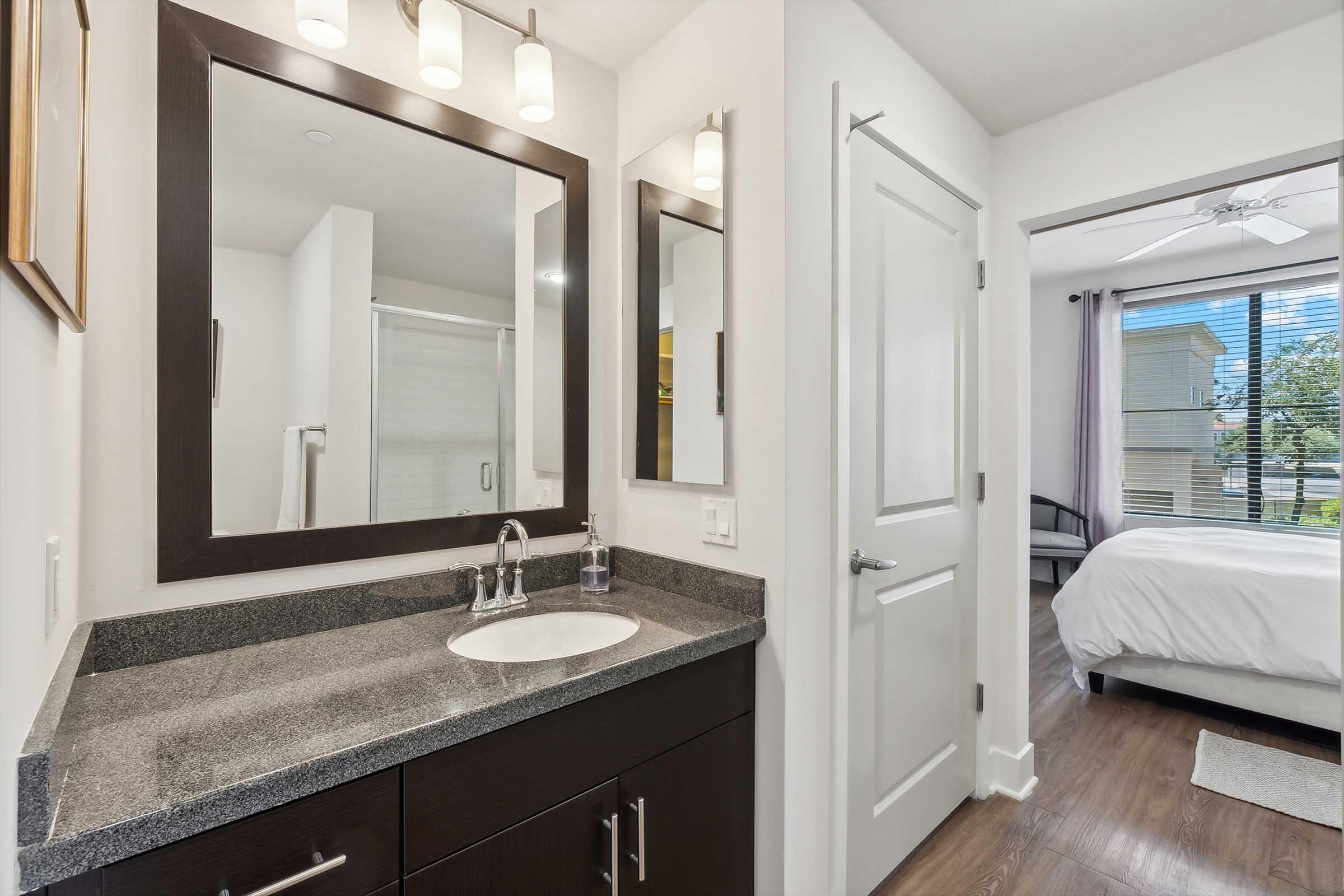 Modern bathroom featuring a dark wood vanity with a granite countertop and sink, a large mirror with overhead lighting, and a sliding glass shower door.
