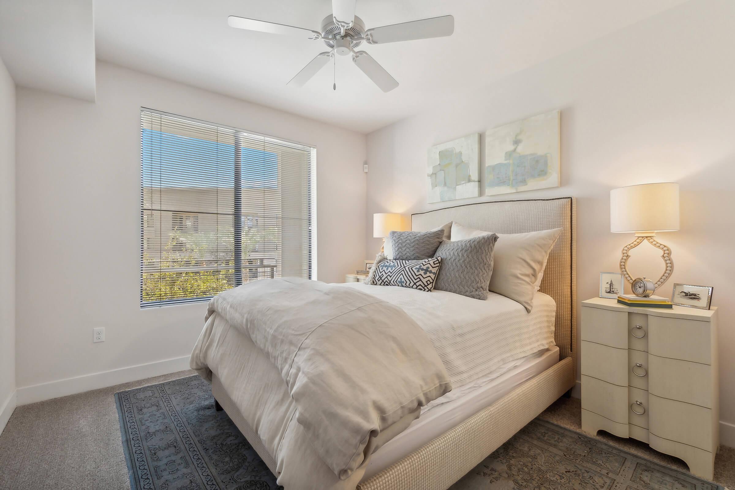 Cozy bedroom featuring a light-colored bed with decorative pillows, bedside tables with lamps, and a window with blinds allowing natural light.