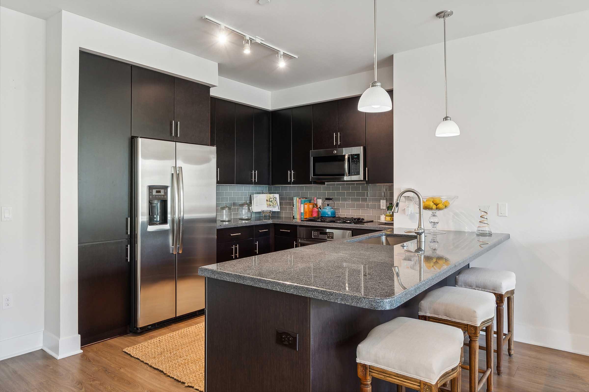 Modern kitchen featuring dark cabinetry, stainless steel appliances, and a large gray countertop with bar stools.