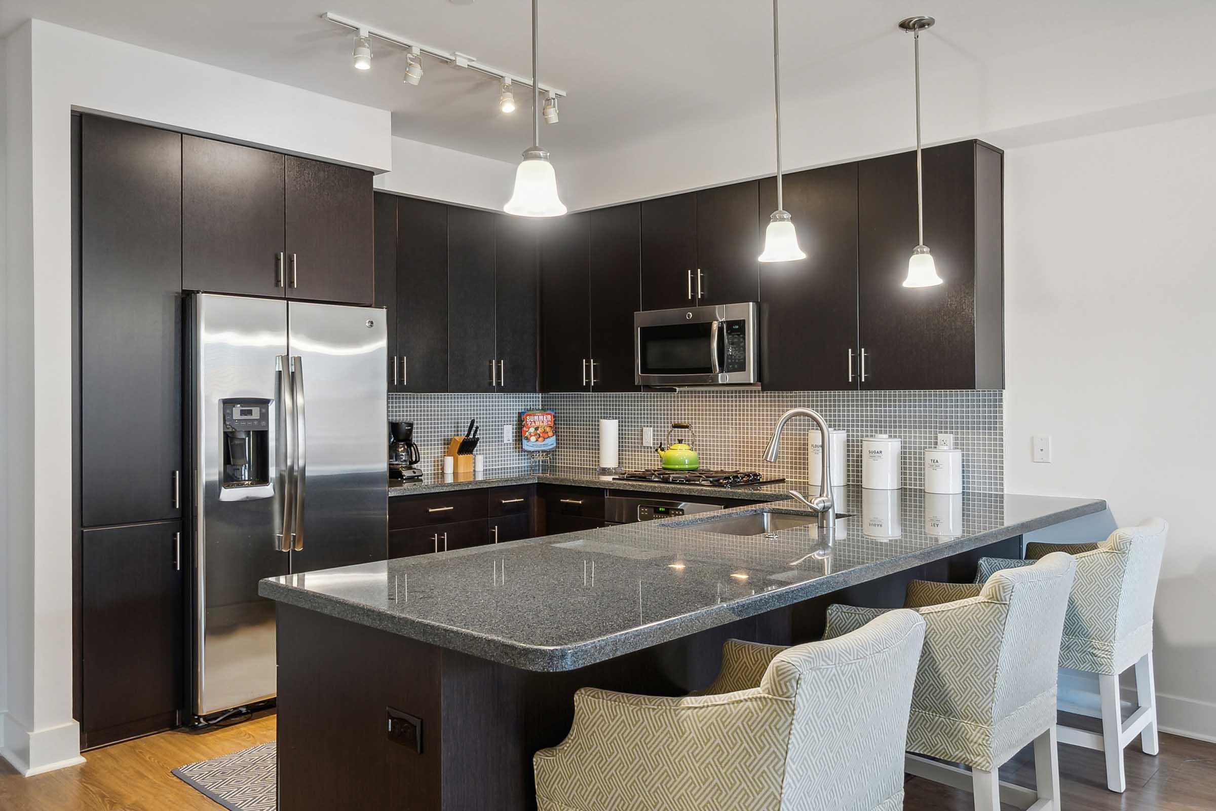 Modern kitchen featuring dark cabinetry, stainless steel appliances, and a gray granite countertop.