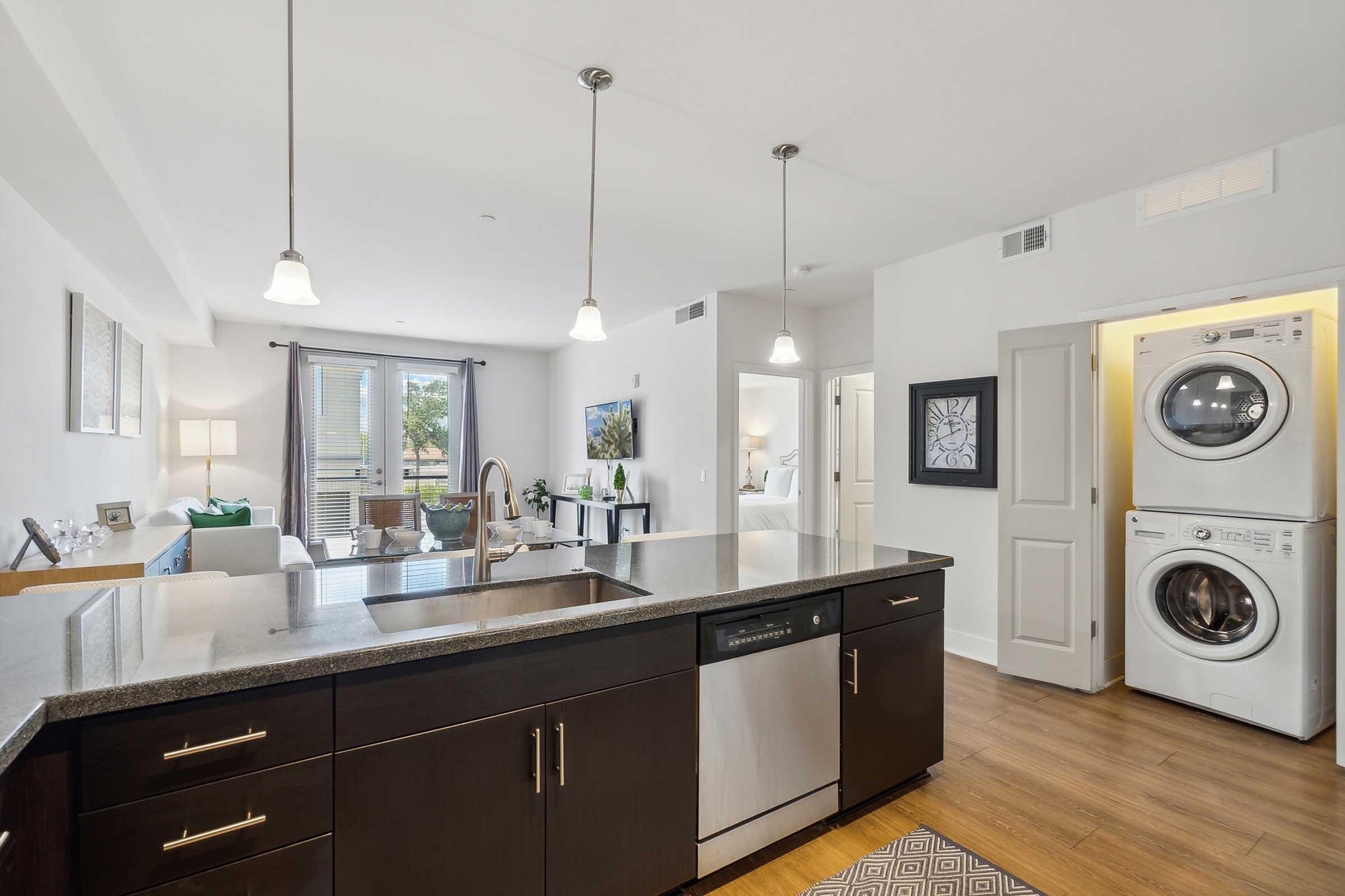 A modern kitchen featuring a dark wood island with a sink and dishwasher. Pendant lights hang above the island.