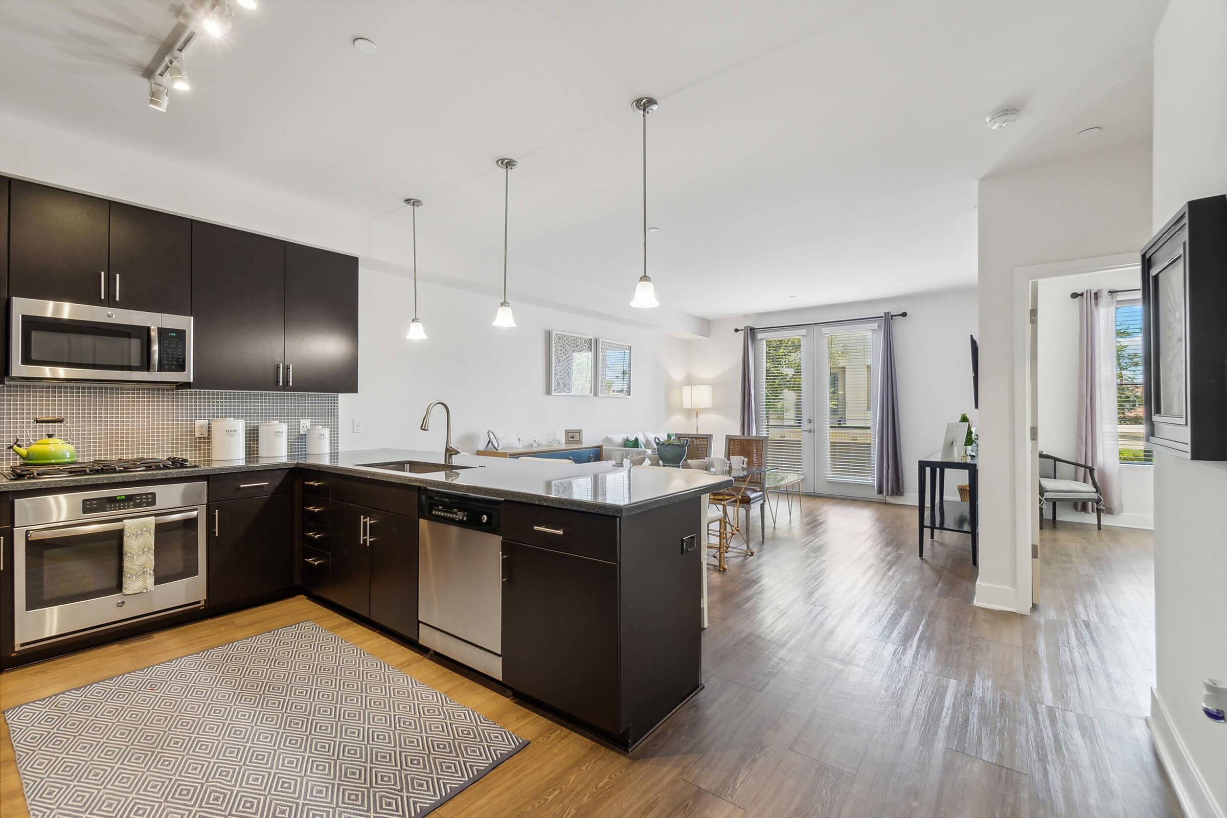 Modern kitchen featuring dark cabinetry, stainless steel appliances, a large island with a countertop, and pendant lighting.