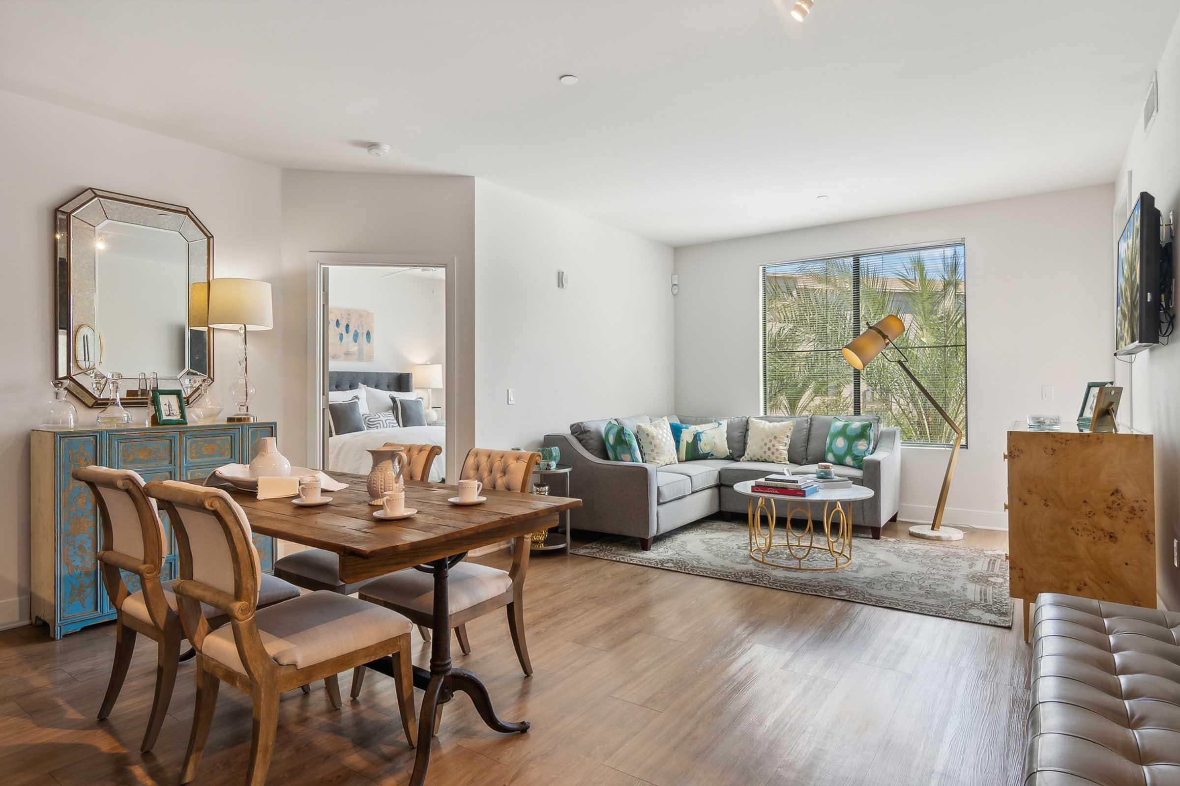 A modern living space featuring a dining table set for four, a cozy gray sofa adorned with colorful pillows, a decorative mirror, and a stylish coffee table.