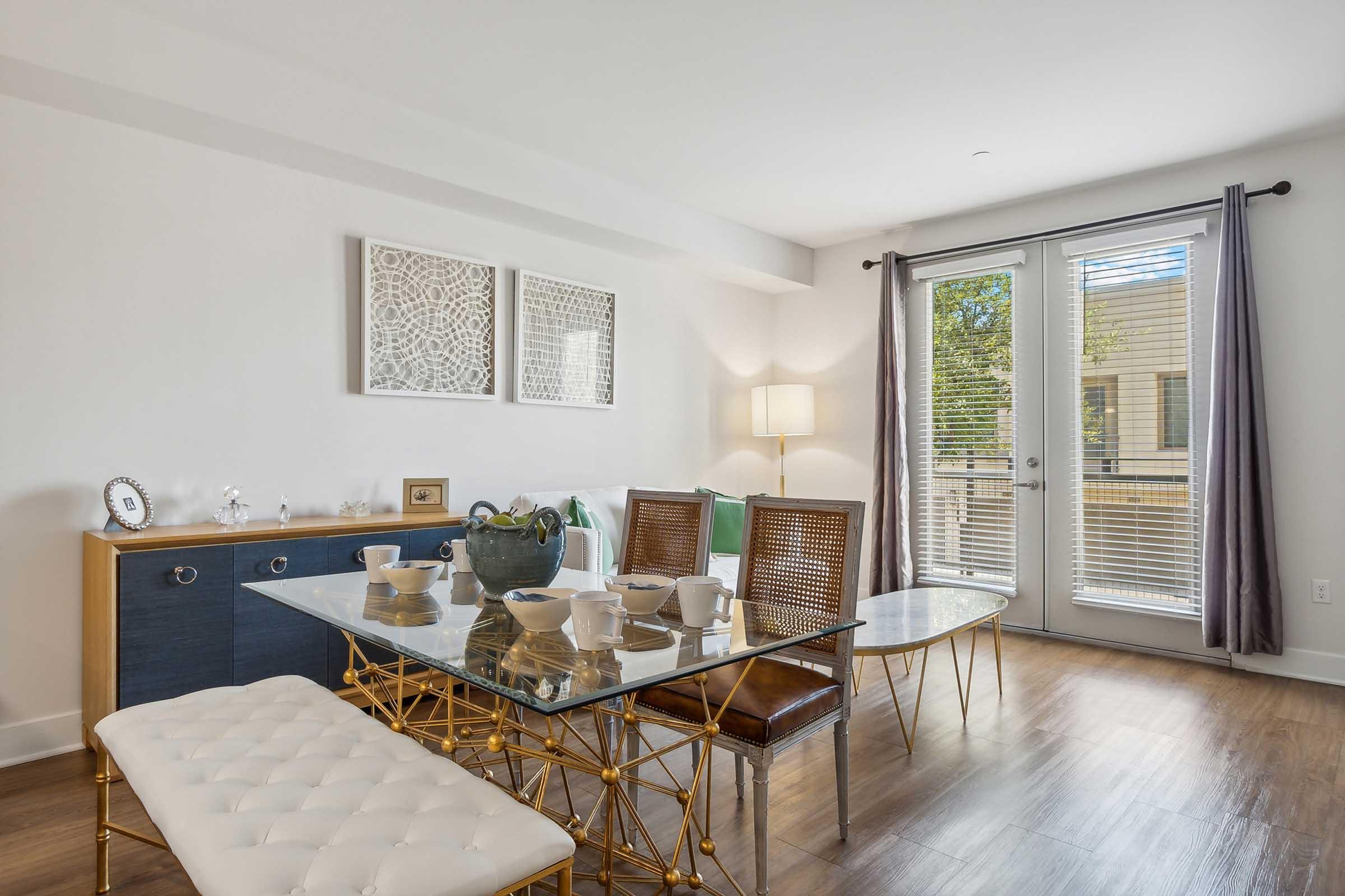 A modern living space featuring a dining table set with white dishware, a glass top coffee table, and stylish seating.