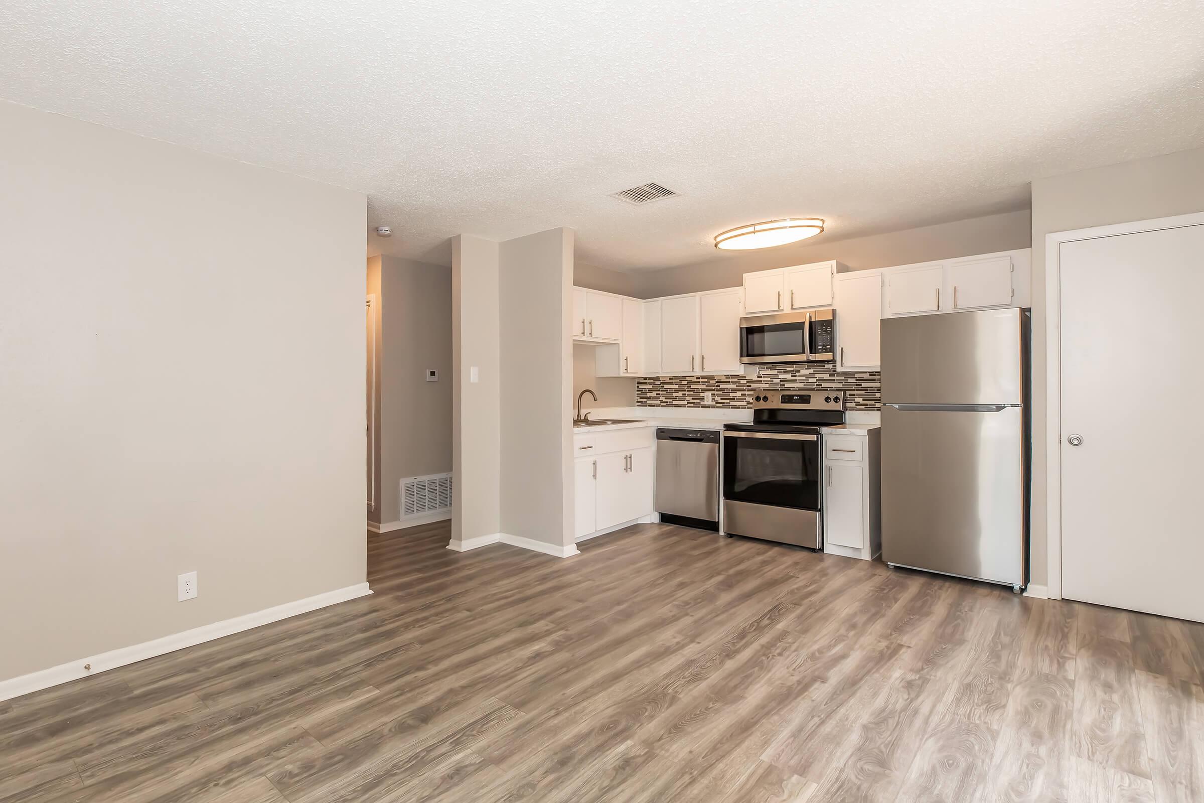 Modern kitchen in a well-lit apartment featuring stainless steel appliances, a tile backsplash, and light wood floors. The open layout includes white cabinetry, a spacious countertop, and an entrance to a hallway. The overall design is contemporary and inviting.