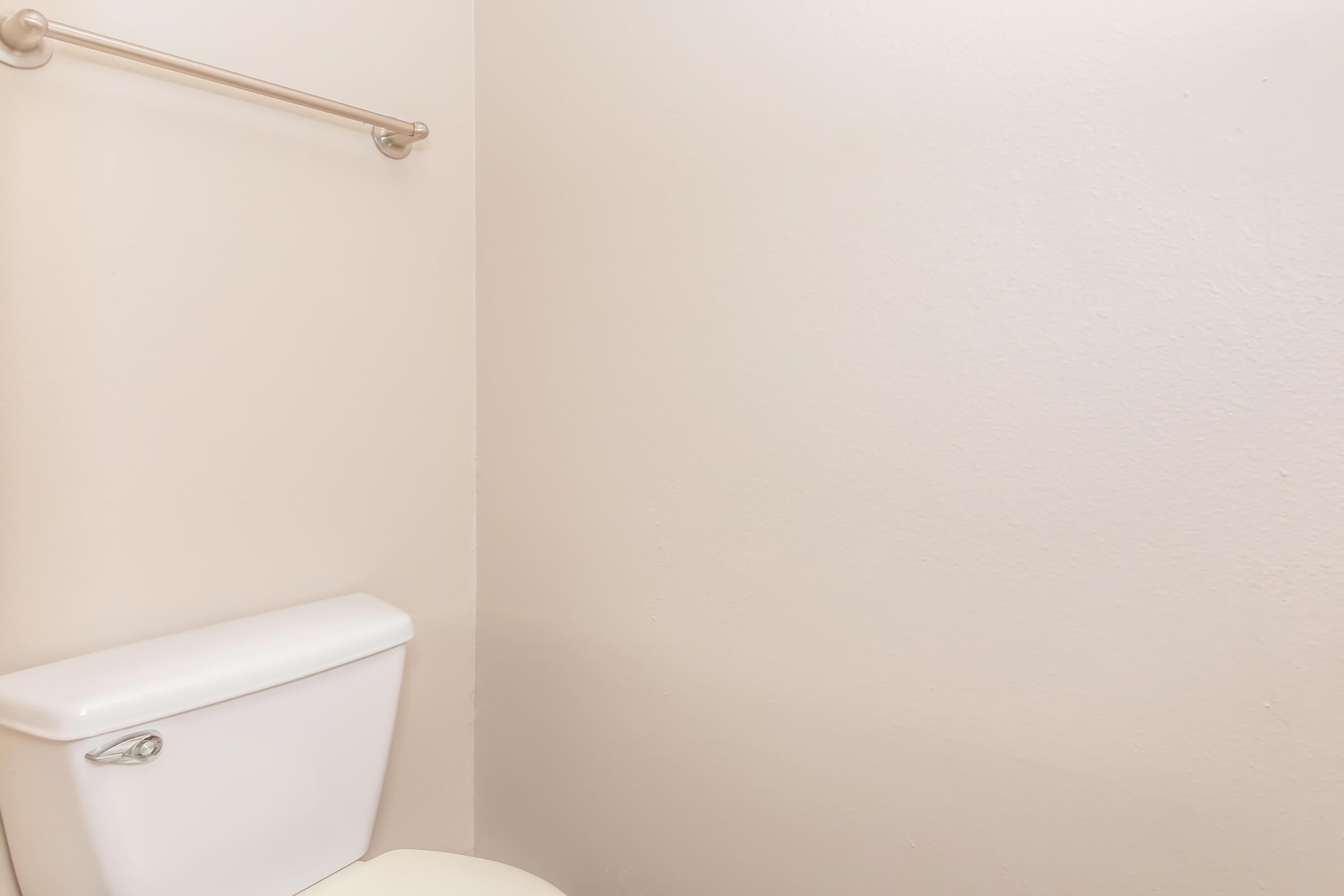 A clean bathroom featuring a white toilet with a silver towel bar mounted on a light-colored wall. The space is simple and uncluttered, emphasizing a minimalist design.