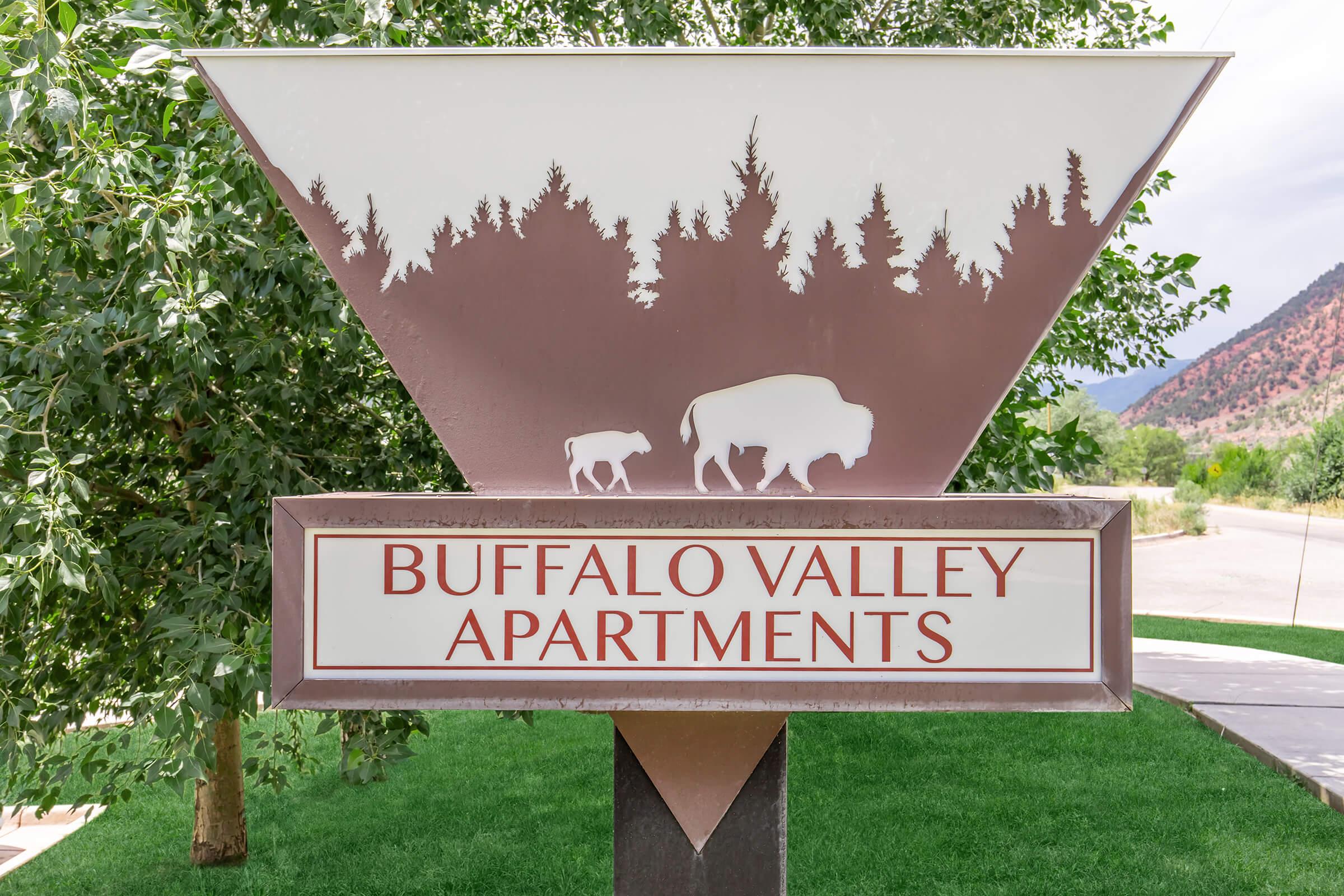 Sign for Buffalo Valley Apartments featuring a stylized depiction of a buffalo and its calf, surrounded by trees and mountains in the background. The design combines natural imagery with text indicating the apartment name.