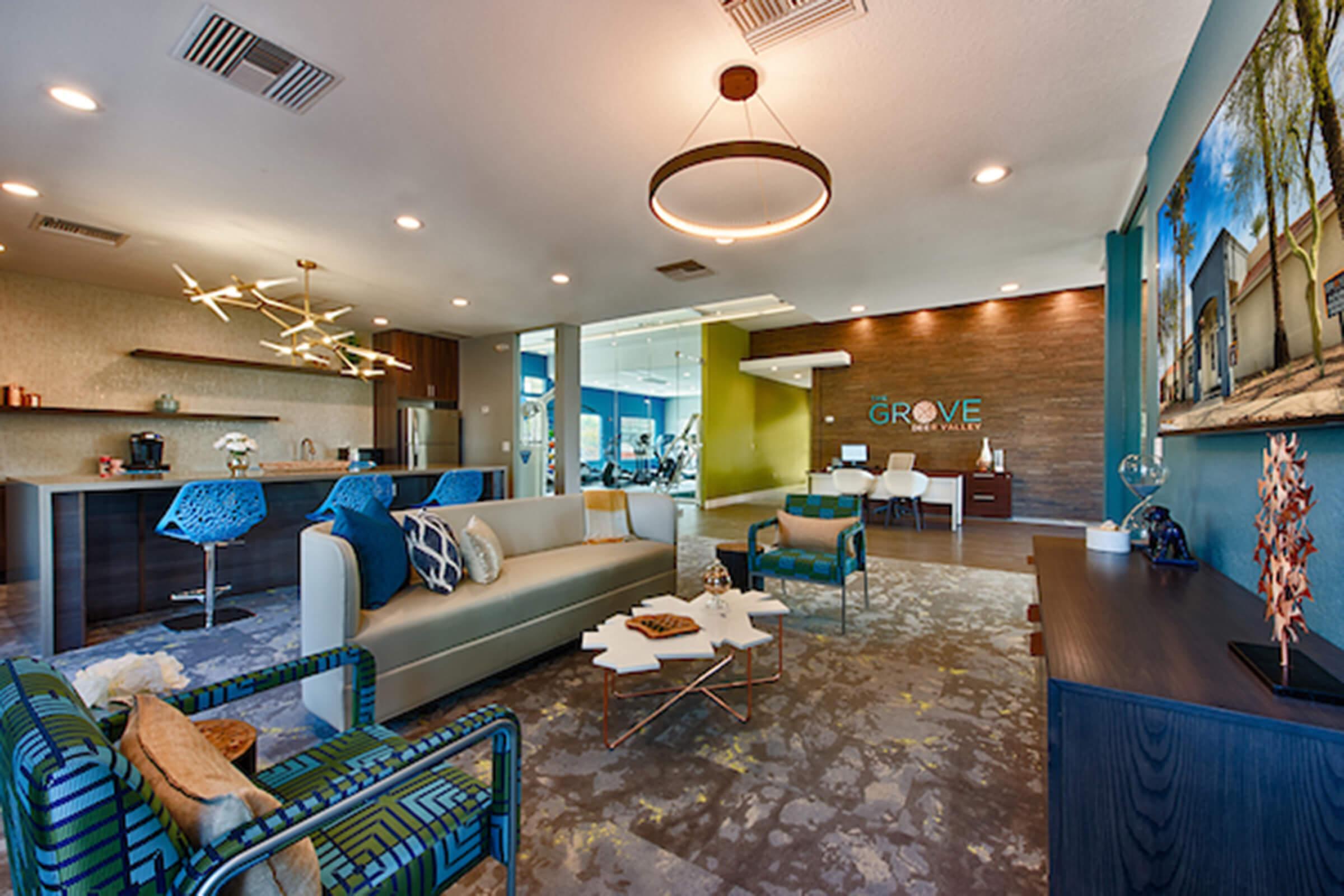 Modern interior of a stylish office reception area featuring comfortable seating, decorative tables, and a green accent wall. A stylish light fixture hangs from the ceiling, and large windows offer ample natural light. The design includes contemporary art pieces and a welcoming atmosphere.