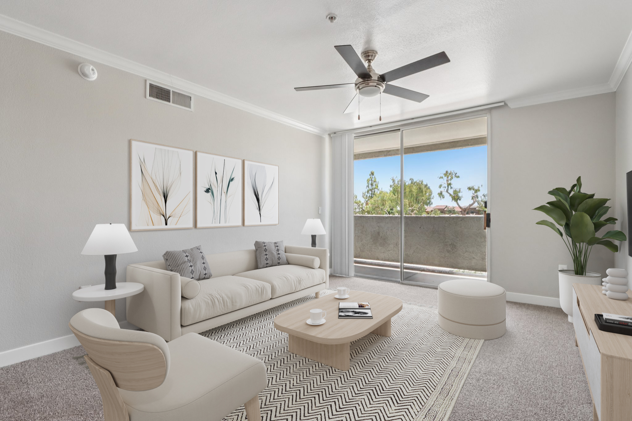 A modern living room featuring a light-colored sofa with decorative pillows, a round coffee table, and a stylish armchair. White lamps flank the sofa, and a large window provides natural light and a view of greenery outside. The walls are painted in neutral tones, complemented by minimalistic artwork.