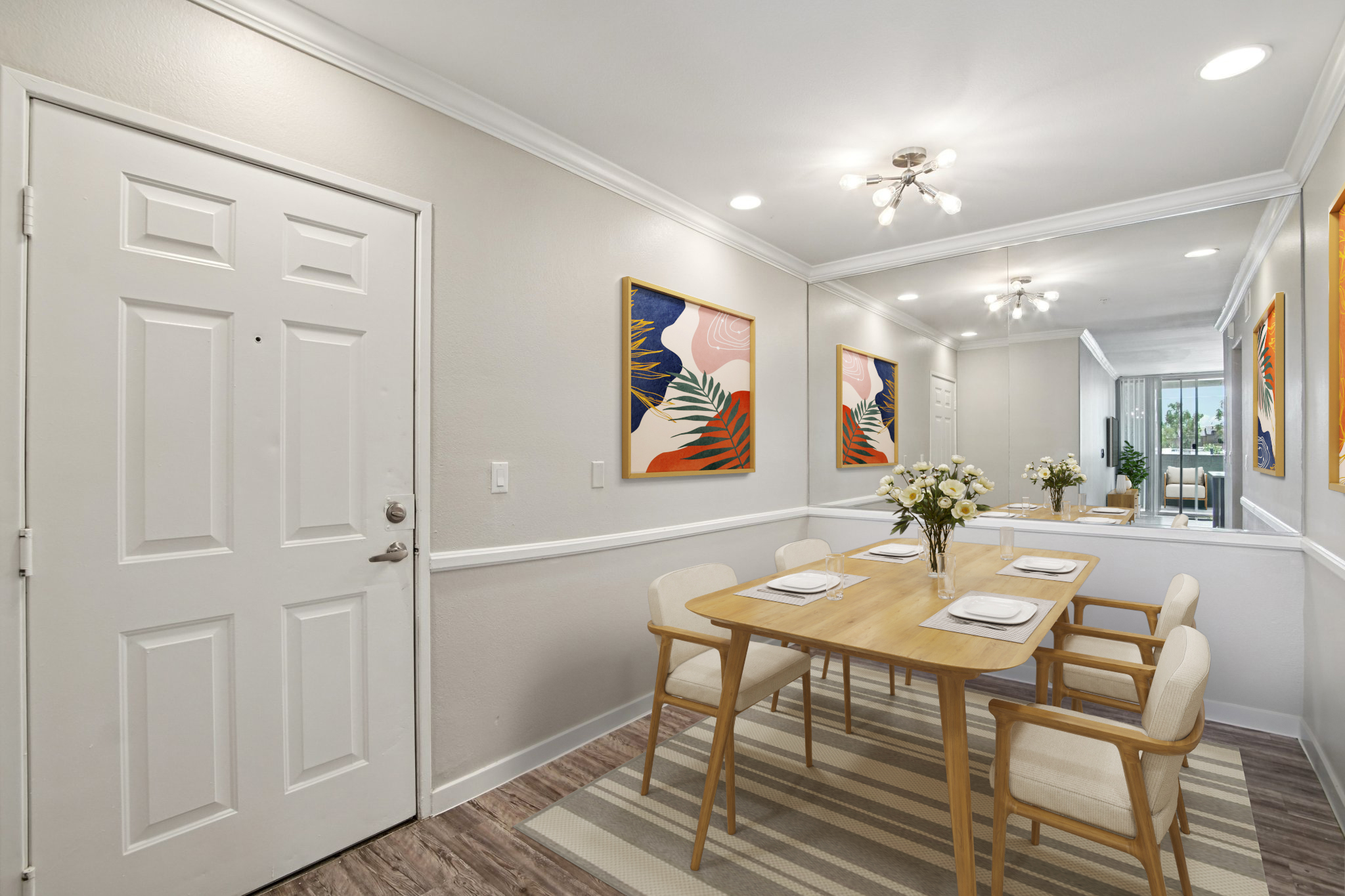 A bright and inviting dining area featuring a wooden table set for four, with light-colored chairs. Two colorful abstract paintings adorn the walls, and a vase of flowers sits on the table. The space has a modern design, with soft lighting and a stylish rug, creating a warm and welcoming atmosphere.