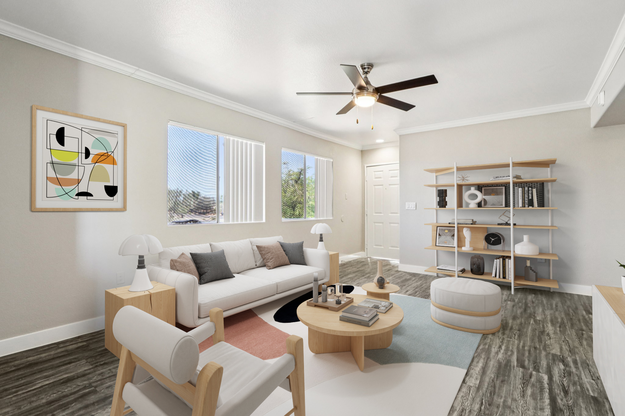 A modern living room featuring a white sofa with black and pastel pillows, a round wooden coffee table, and a light-colored armchair. The room has large windows allowing natural light, a ceiling fan, and decorative shelves with various items. A colorful abstract art piece is on the wall, enhancing the contemporary feel.