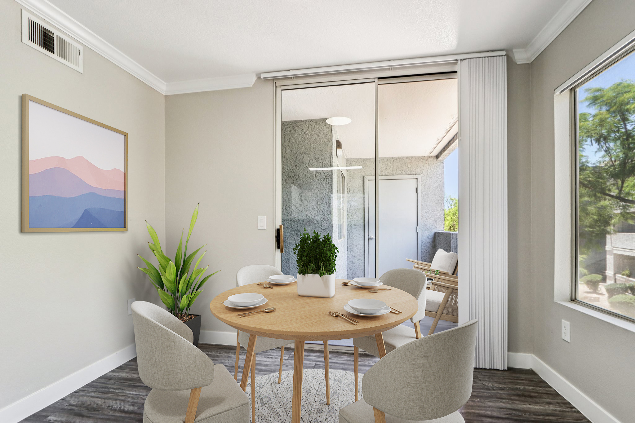 A modern dining area featuring a round wooden table set for four with plates and a centerpiece of greenery. Light-colored walls and a large window provide natural light, while a sliding glass door opens to an outdoor space. A minimalist artwork hangs on the wall, and potted plants add a touch of nature.