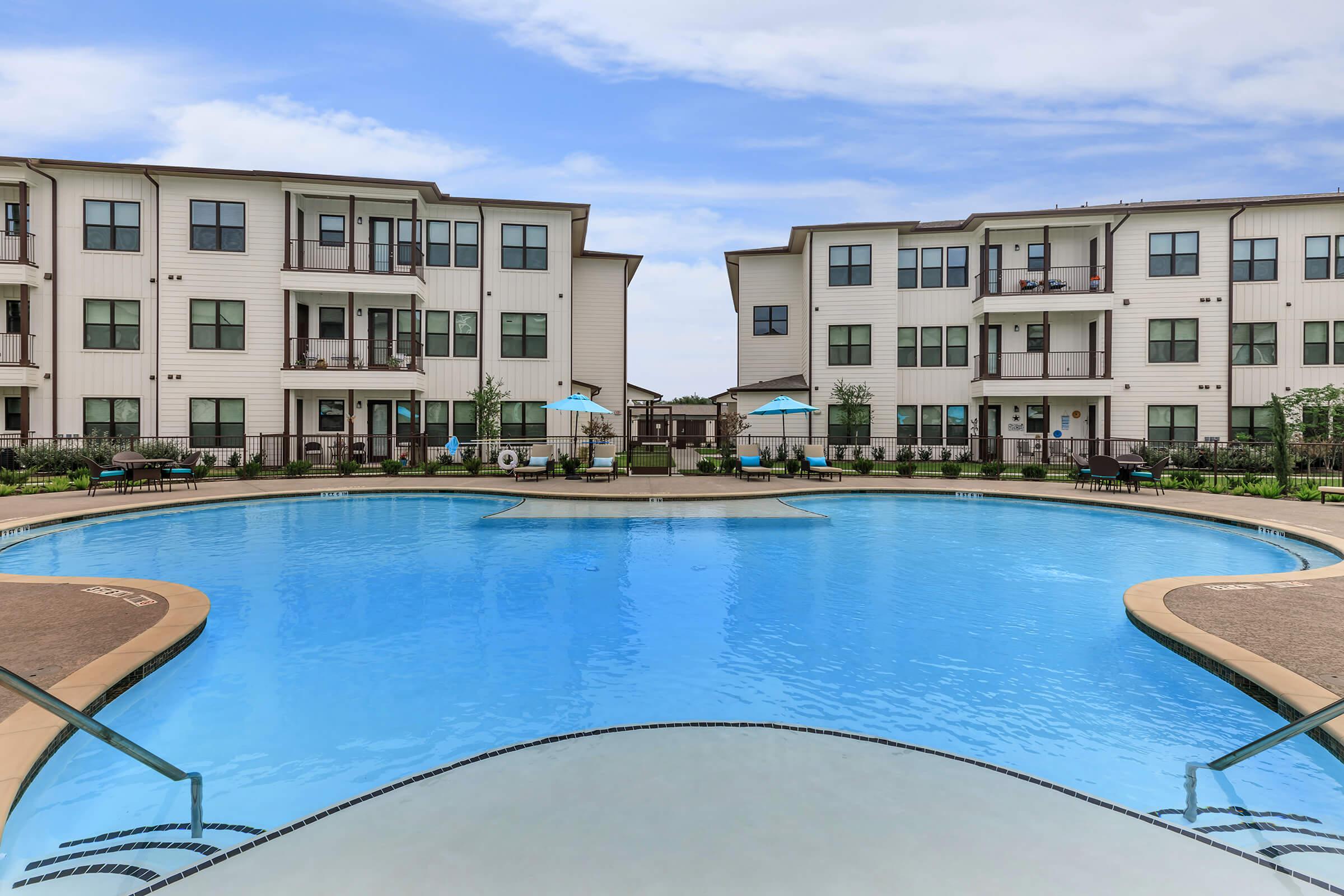 The pool area at our senior living apartments in Spring, TX, featuring umbrellas, lounge chairs, and