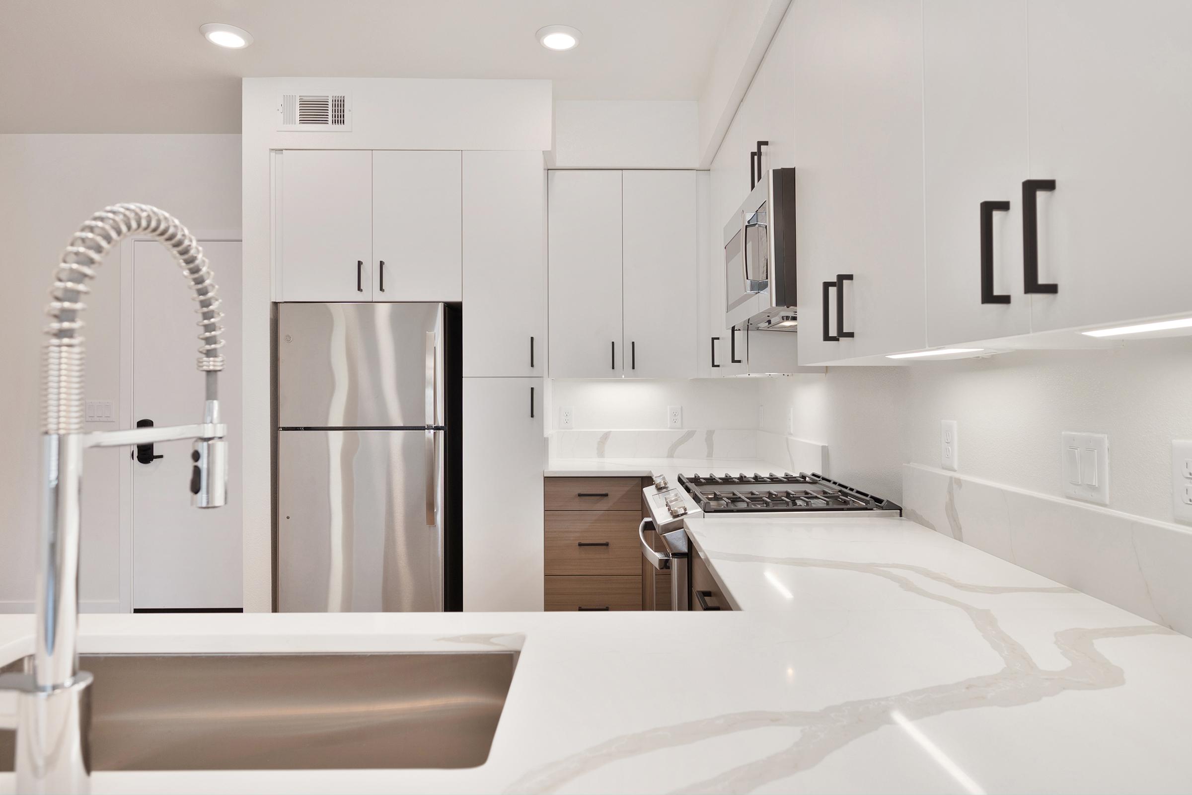Modern kitchen featuring sleek white cabinets with black handles, a stainless steel refrigerator, and a gas stove. The kitchen island has a large sink with a modern faucet, and the countertop showcases a light-colored marble design, creating a bright and contemporary ambiance.