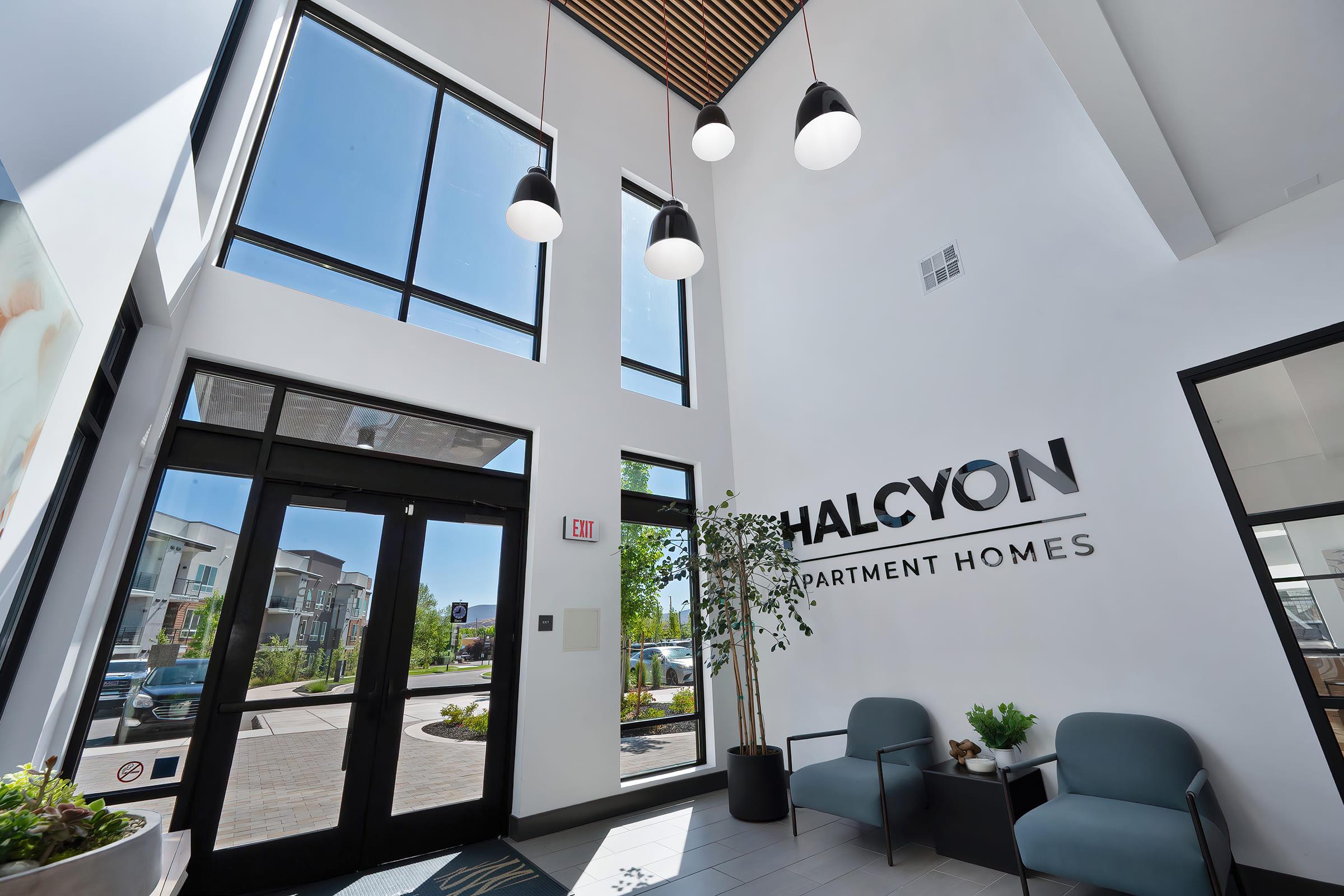 Bright and modern lobby of Halcyon Apartment Homes featuring large windows, pendant lighting, and a sleek design. There are two comfortable chairs and a welcoming atmosphere, creating an inviting entryway for residents and guests.