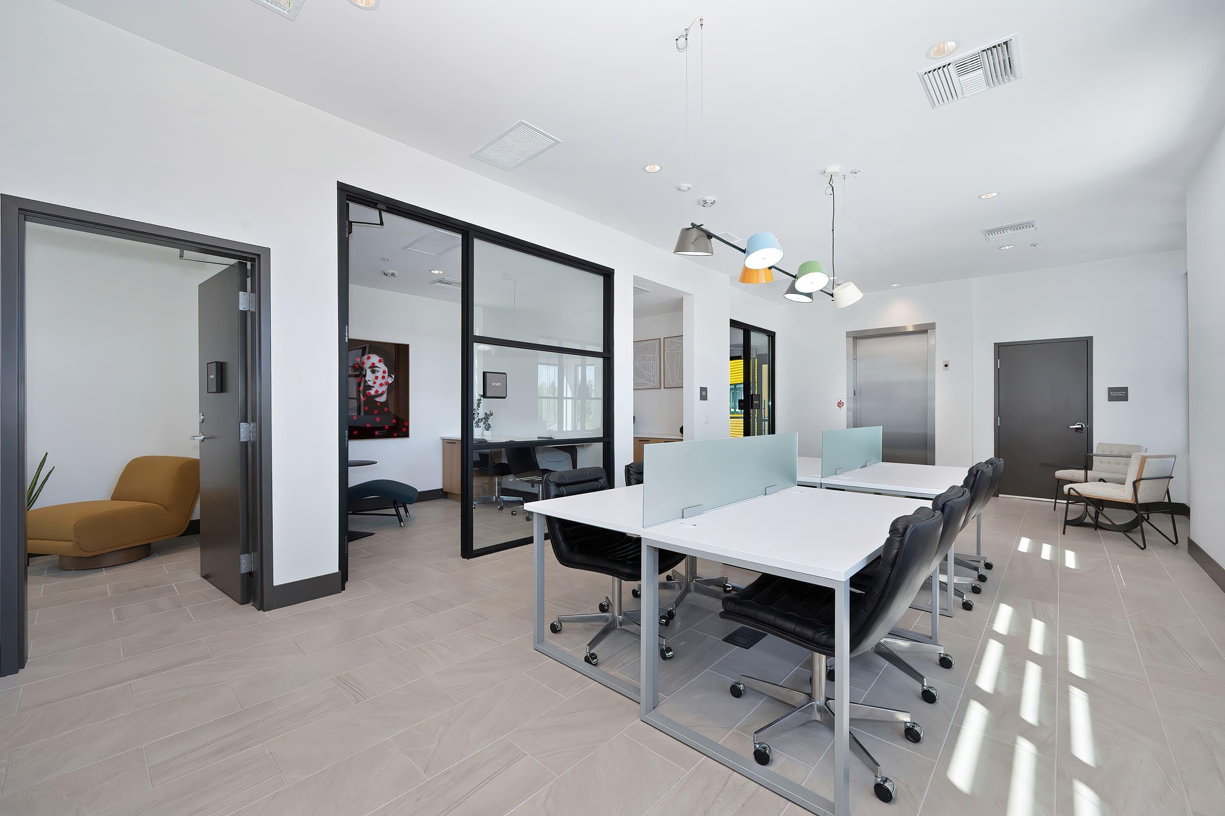 A modern office interior featuring a spacious layout with glass walls, multiple desks with ergonomic chairs, and contemporary lighting. There is a cozy seating area with an orange chair and a wall art piece in the background. The floor is tiled in a light color, creating a bright and inviting atmosphere.