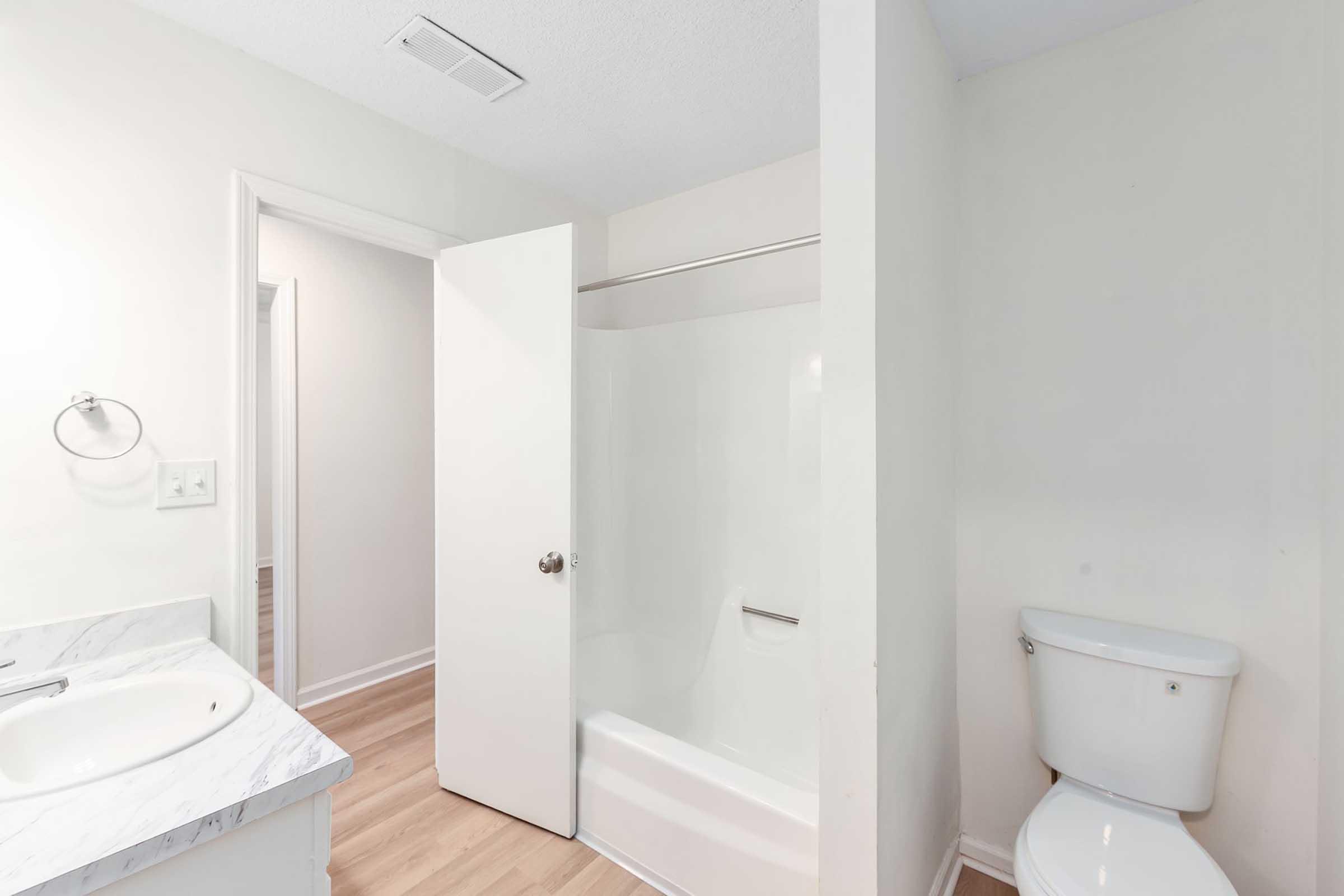 A clean and bright bathroom featuring a white bathtub and shower combo, a modern sink with a marble countertop, and a toilet. The walls are painted in light colors, and the flooring is light wood, creating a spacious and inviting atmosphere.