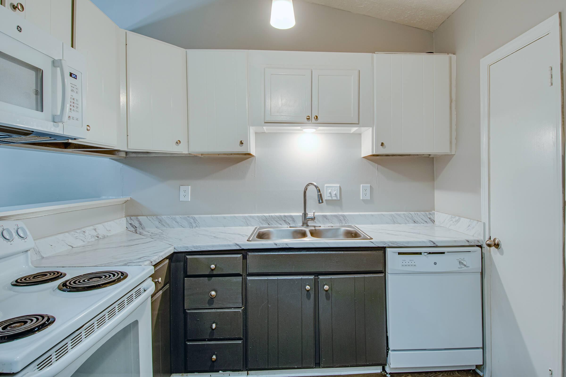 A modern kitchen featuring white and dark cabinets, a double sink with a marble countertop, an electric stove, microwave, and a dishwasher. The kitchen has neutral-colored walls and a pendant light overhead, creating a clean and functional space.