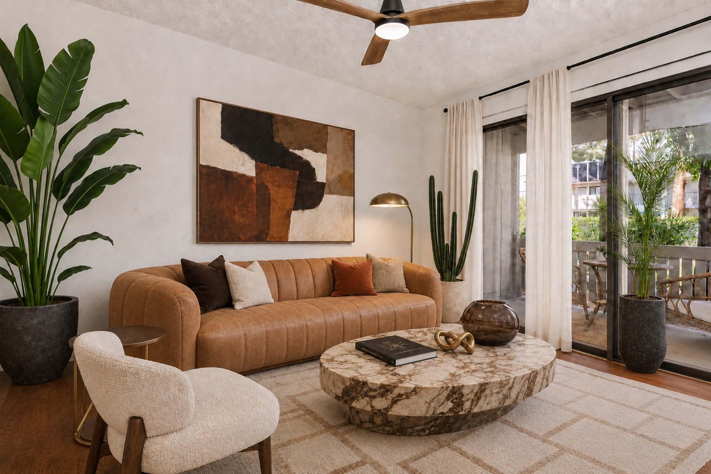 A modern living room featuring a brown leather sofa adorned with decorative pillows, a round marble coffee table, and a stylish floor lamp. Large plants are positioned nearby, and expansive glass doors lead to an outdoor space, enhancing the bright and inviting atmosphere.