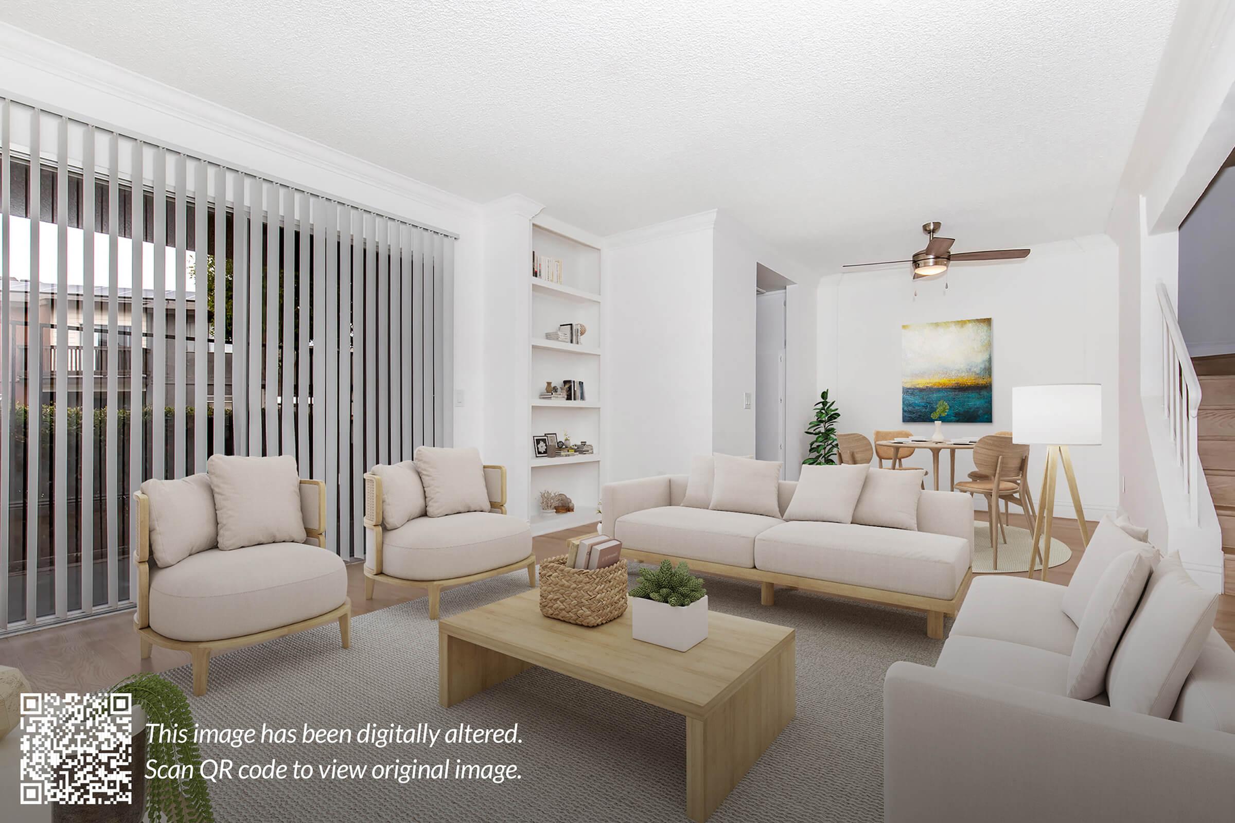A bright, modern living room featuring light-colored furniture, including two armchairs and a sofa, arranged around a wooden coffee table. There are shelves with decorative items on one side, and a painting on the wall. Large sliding glass doors lead to an outdoor area, with natural light filling the space.