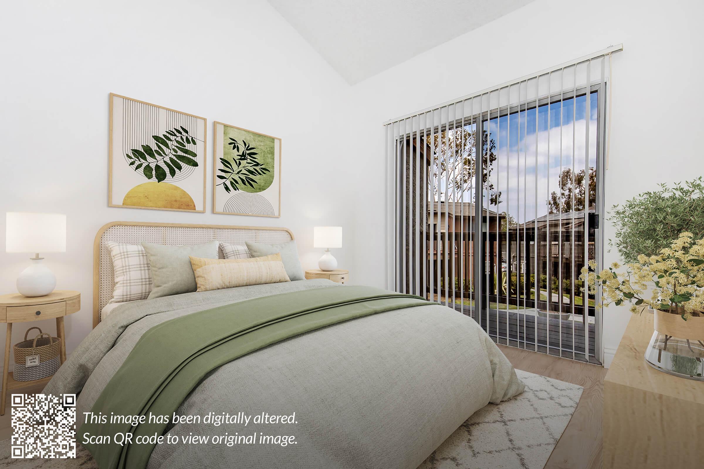 A cozy bedroom featuring a neutral color palette with a large bed dressed in soft linens and a green throw. Two framed botanical prints adorn the wall above the bed. Natural light filters through vertical blinds, showing a view of an outdoor scene. A nightstand on each side holds decorative lamps. A plant and flowers are placed on a wooden dresser.