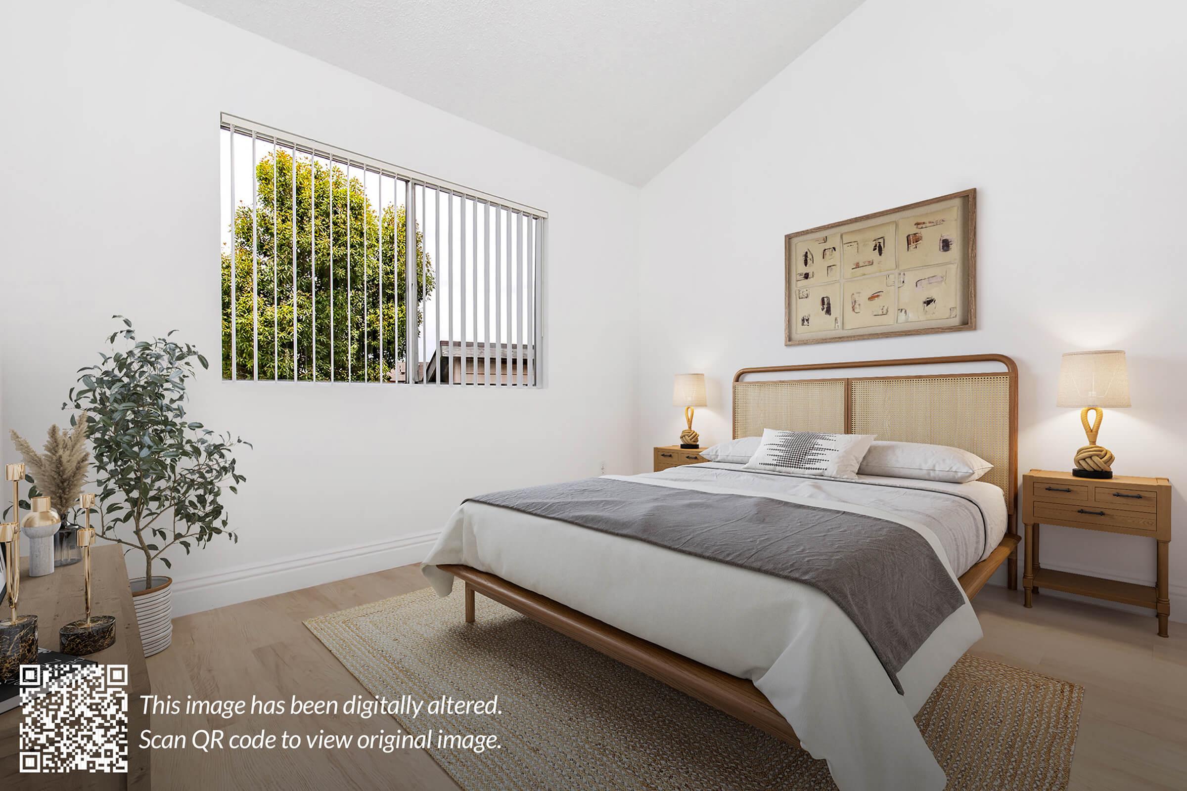 A well-lit bedroom featuring a wooden bed with white and gray bedding, two wooden nightstands on either side, and a decorative wall frame. Large windows with vertical blinds allow natural light to enter. A potted plant and decorative vase add a touch of greenery to the minimalist decor.