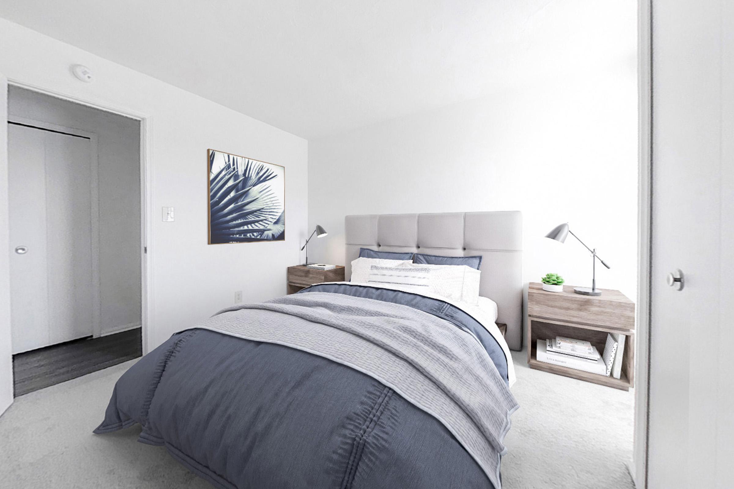 A bright and airy bedroom with light-colored walls and a cozy bed featuring a blue comforter. A small bedside table with a lamp is on either side of the bed, and a piece of wall art with a leaf design hangs above. A closet door is visible on the left side of the image.