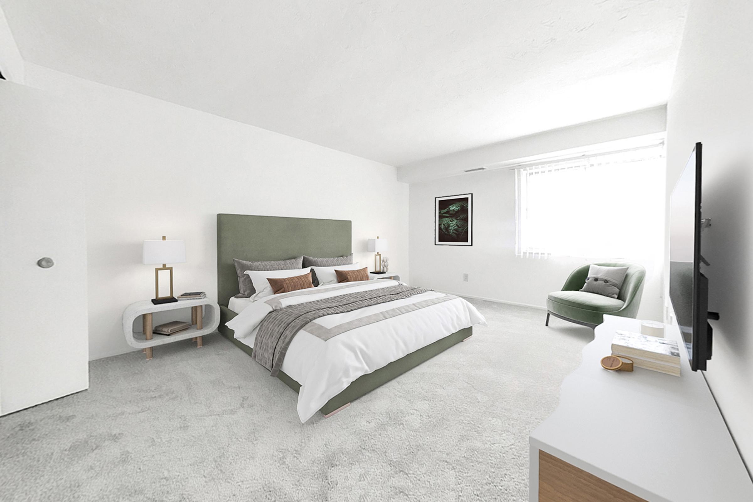 A modern bedroom featuring a large bed with a green headboard, a cozy gray blanket, and decorative pillows. There are two bedside lamps, a comfortable green armchair, a television on a white cabinet, and a window with sheer curtains allowing natural light. The walls and carpet are neutral-toned, creating a serene atmosphere.