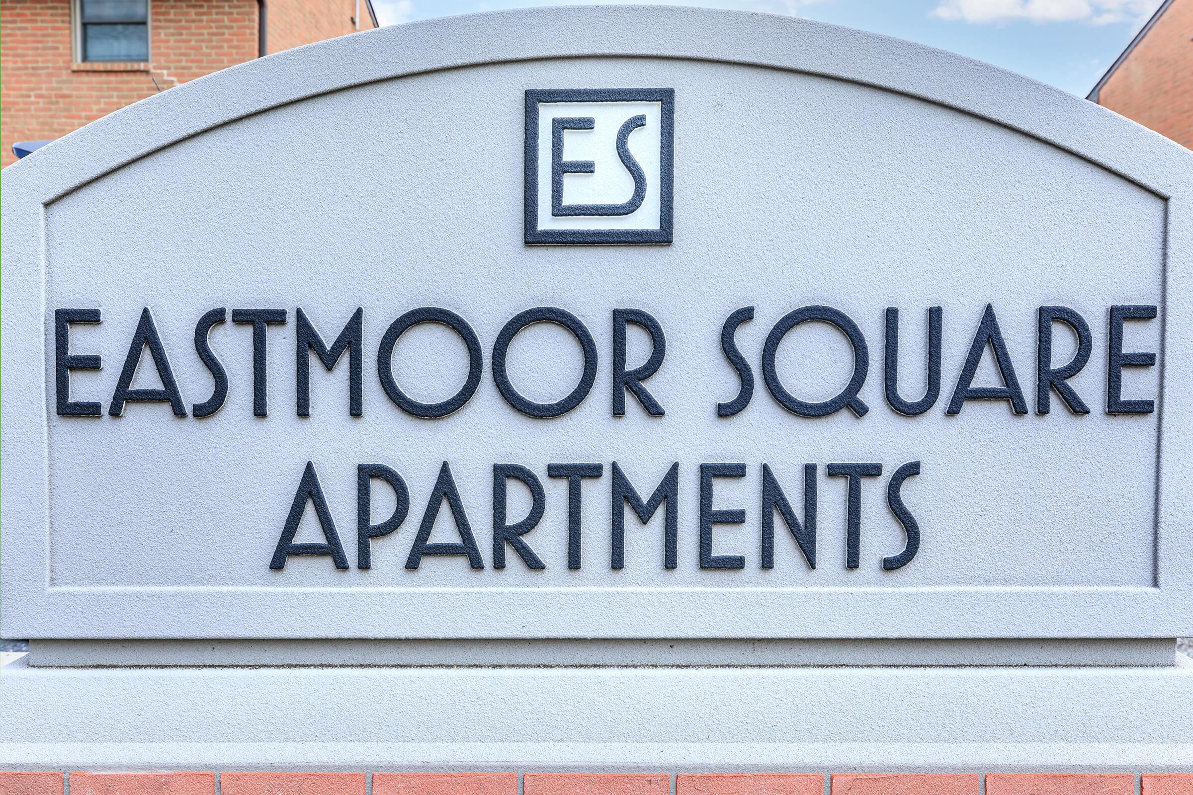 Sign for Eastmoor Square Apartments featuring the initials "ES" at the top. The sign is prominently displayed with a textured stone background.
