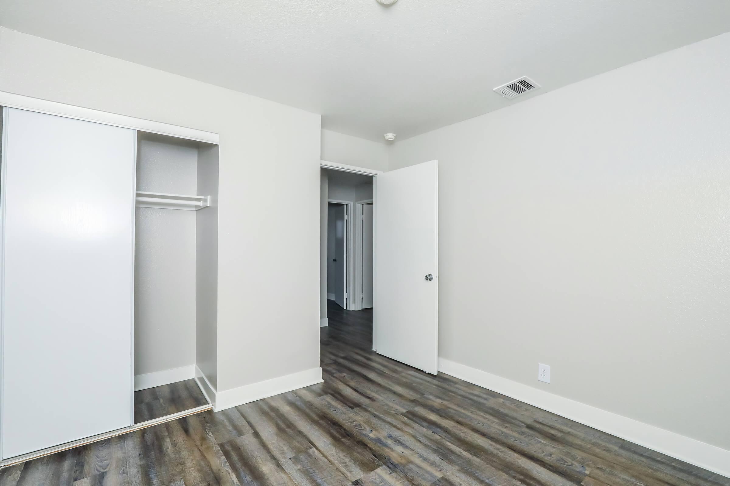 A well-lit interior room featuring a closet with sliding doors, a closed door leading to another space, and hardwood-like flooring. The walls are painted a neutral color, creating a clean and modern look. Ideal for residential or rental listing images.