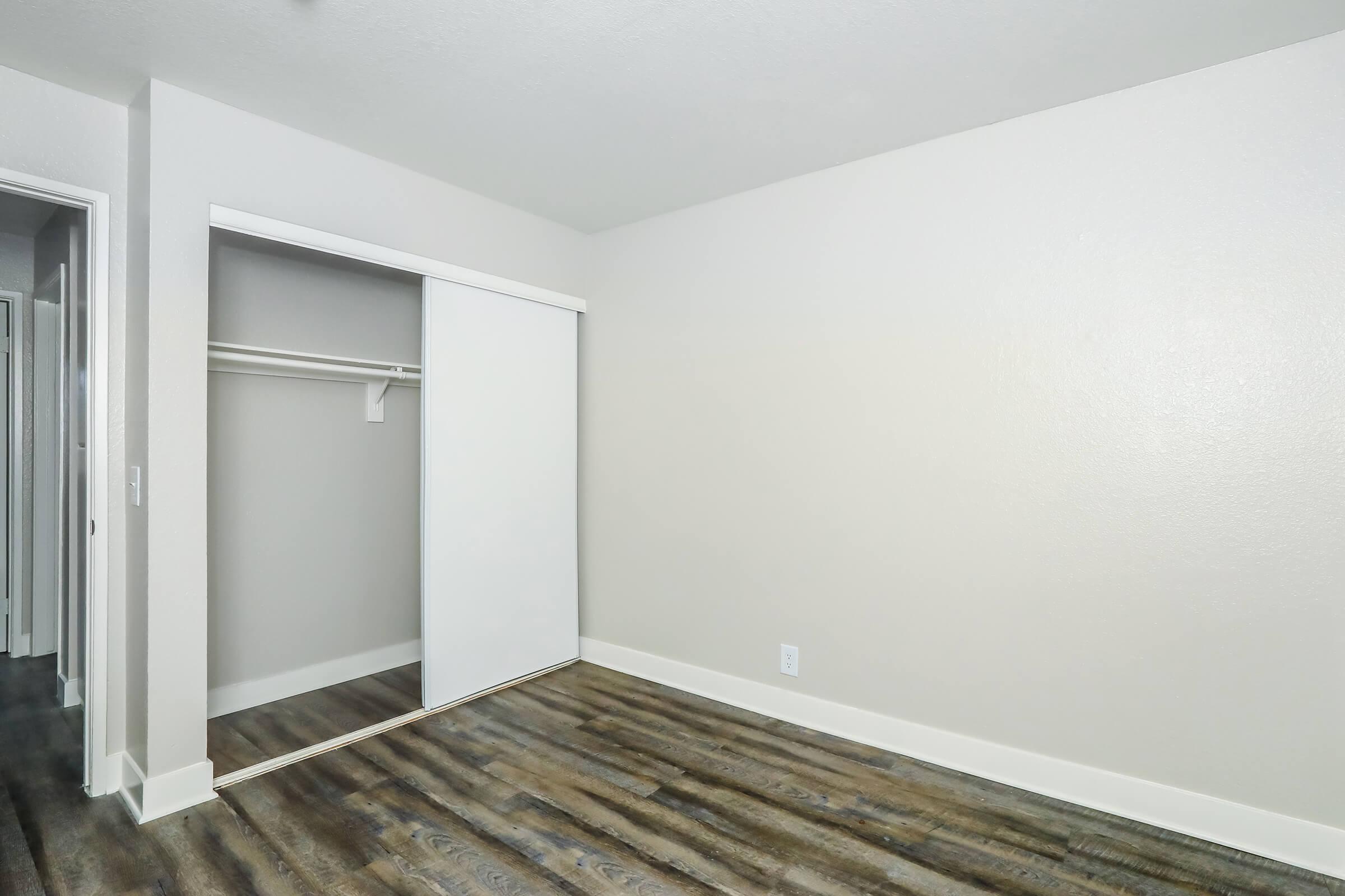 Empty room featuring a light-colored wall with a sliding closet door and wooden flooring. The space appears clean and well-lit, offering potential for personalization and decoration.