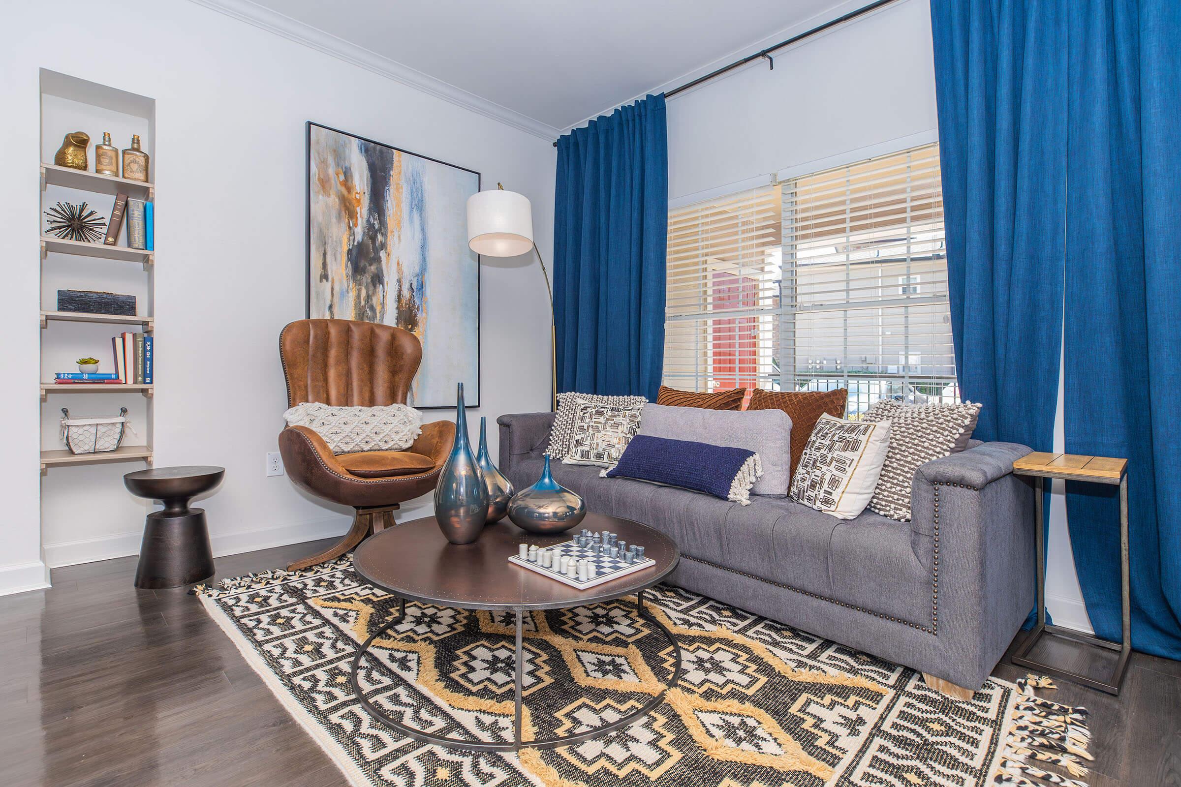 a living room filled with furniture and a rug in front of a curtain