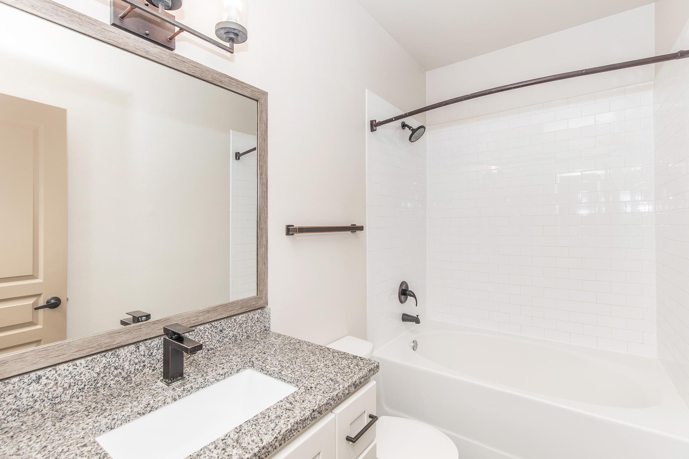 Modern bathroom featuring a white tiled shower with a curved curtain rod, a solid bathtub, a double sink with a sleek faucet, and a large mirror framed with wood. The walls are painted light, and there are minimalistic fixtures, creating a clean and serene atmosphere.