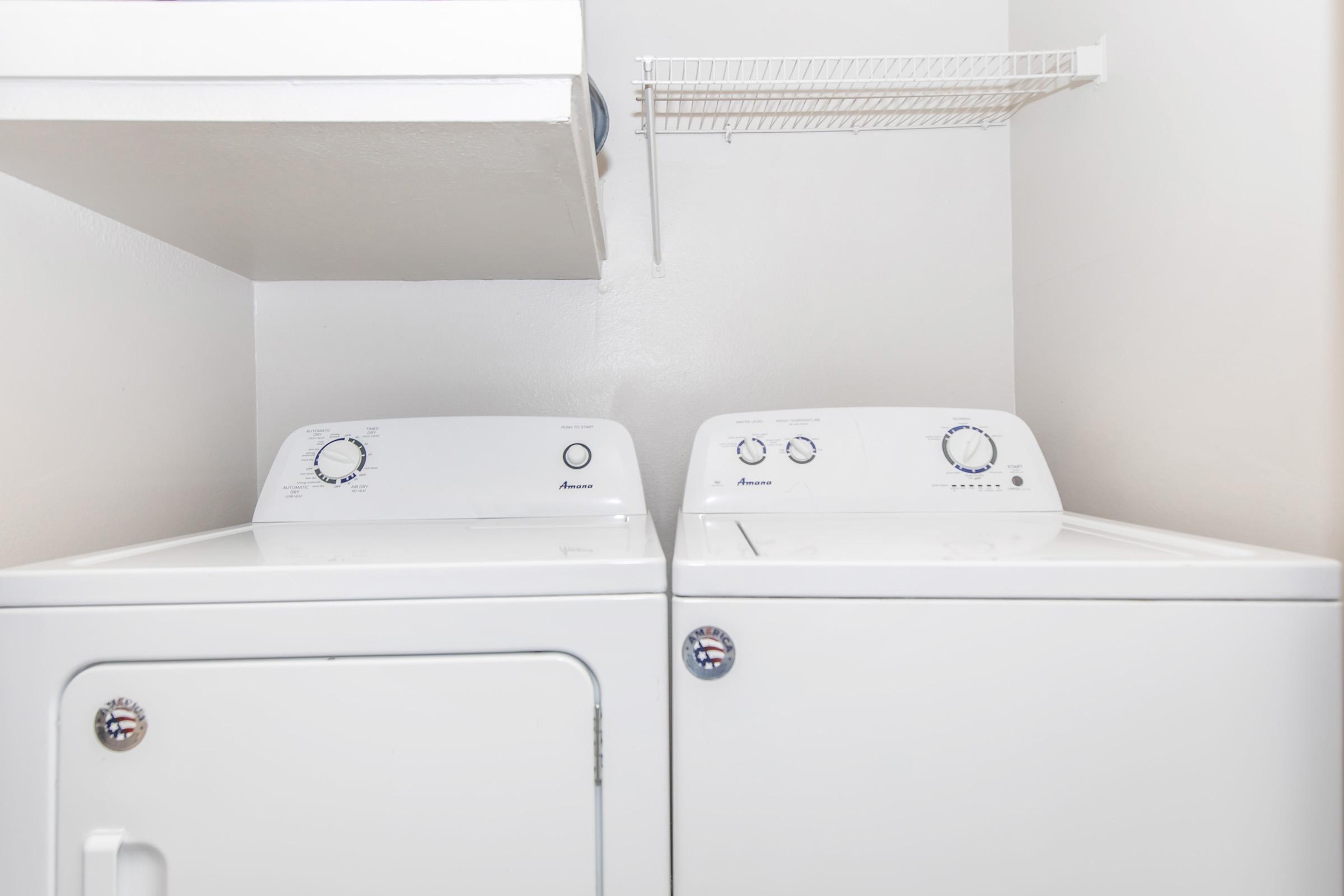 A clean laundry room featuring a white washing machine and dryer side by side. Above them, there's a wire shelf for storage. The walls are painted in a neutral color, creating a bright and organized space for laundry tasks.