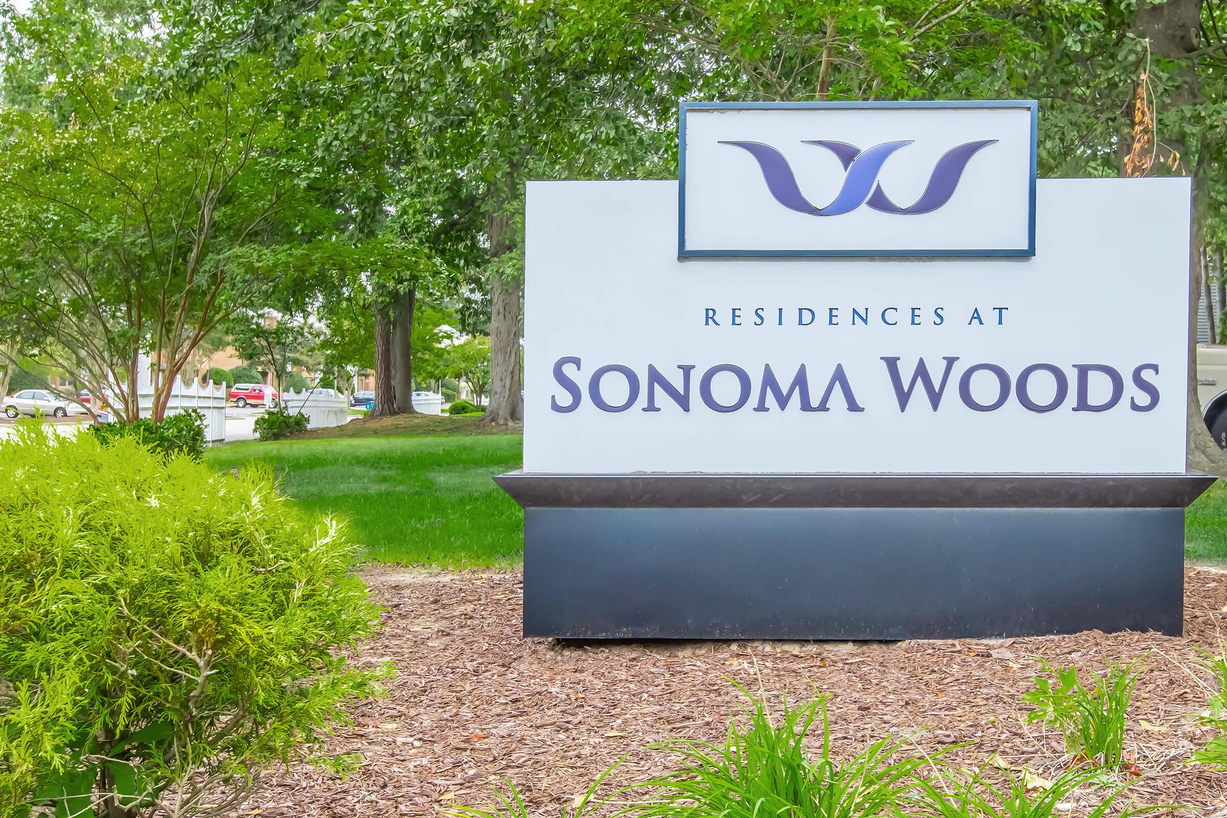 Sign for "Residences at Sonoma Woods" located in a green, landscaped area with trees and bushes surrounding it.