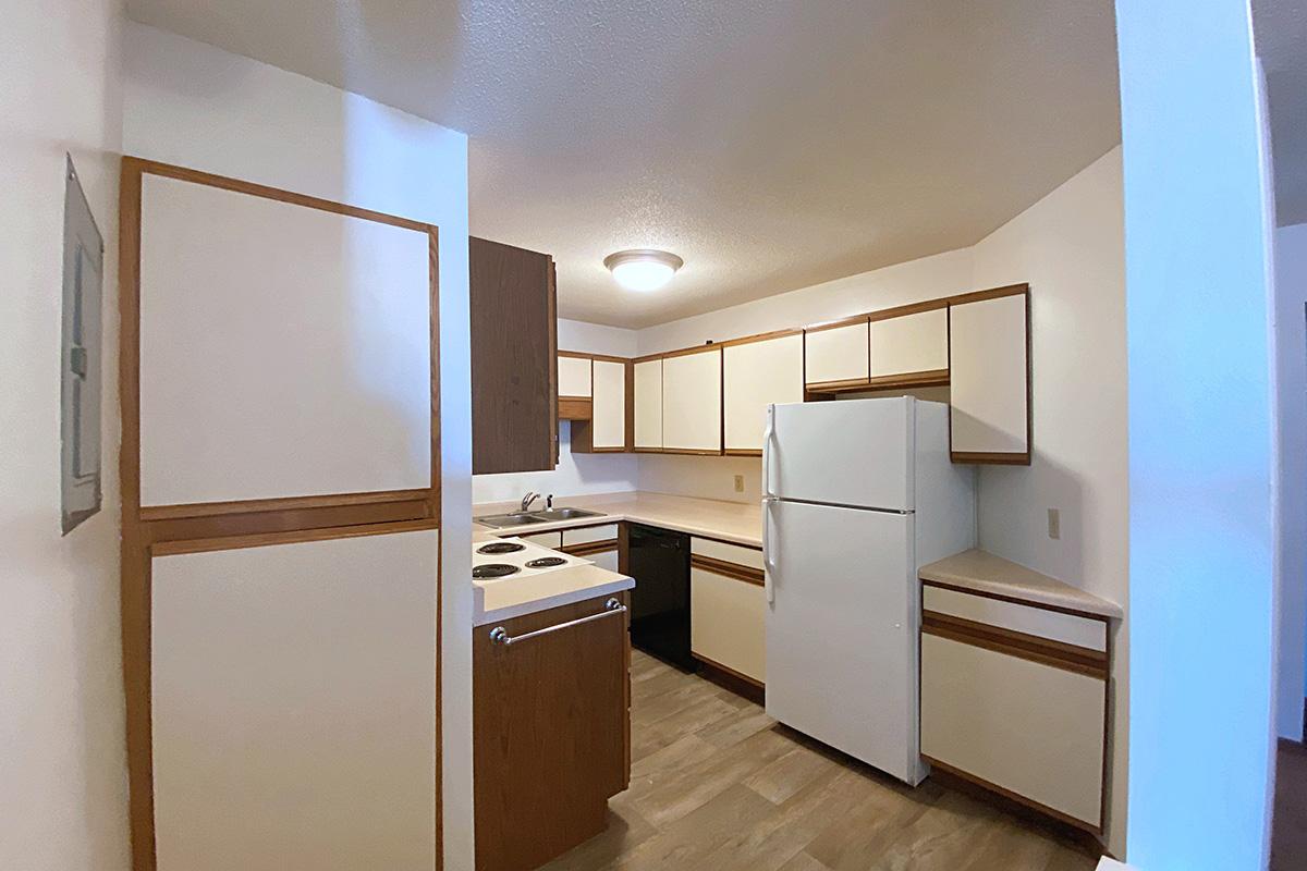 A modern kitchen featuring white cabinets with wood accents, a white refrigerator, a black dishwasher, and a stove with an oven. The countertops are light-colored, and the flooring is a wood-like material. Soft lighting illuminates the space, creating a clean and welcoming atmosphere.