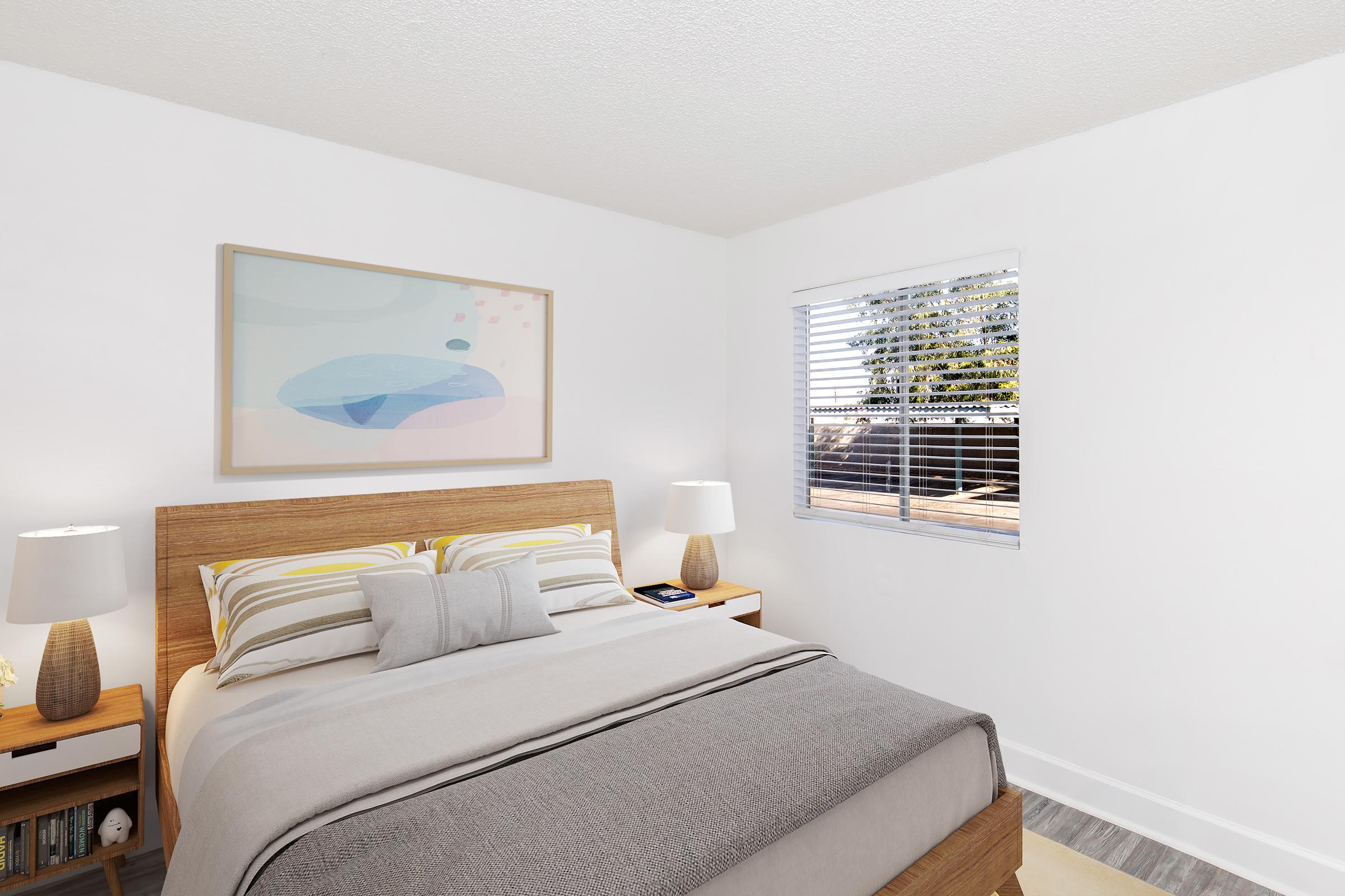 A cozy bedroom featuring a wooden bed with colorful striped bedding, two bedside lamps, and a light gray throw blanket. There's a minimalist artwork above the bed and a window with white blinds letting in natural light, creating a welcoming atmosphere. A glimpse of greenery is visible outside the window.