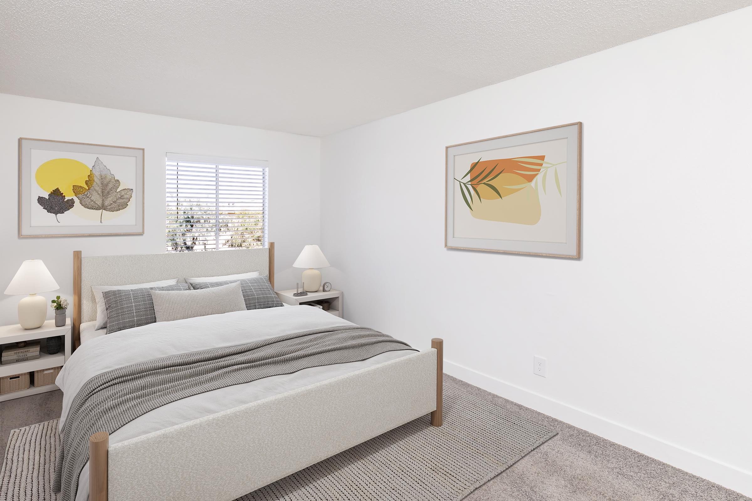 A modern bedroom featuring a light-colored wooden bed with gray bedding, two bedside tables with lamps, and abstract art on the walls. Natural light streams through a window with white blinds, and there is a soft area rug on the floor, creating a cozy and inviting atmosphere.