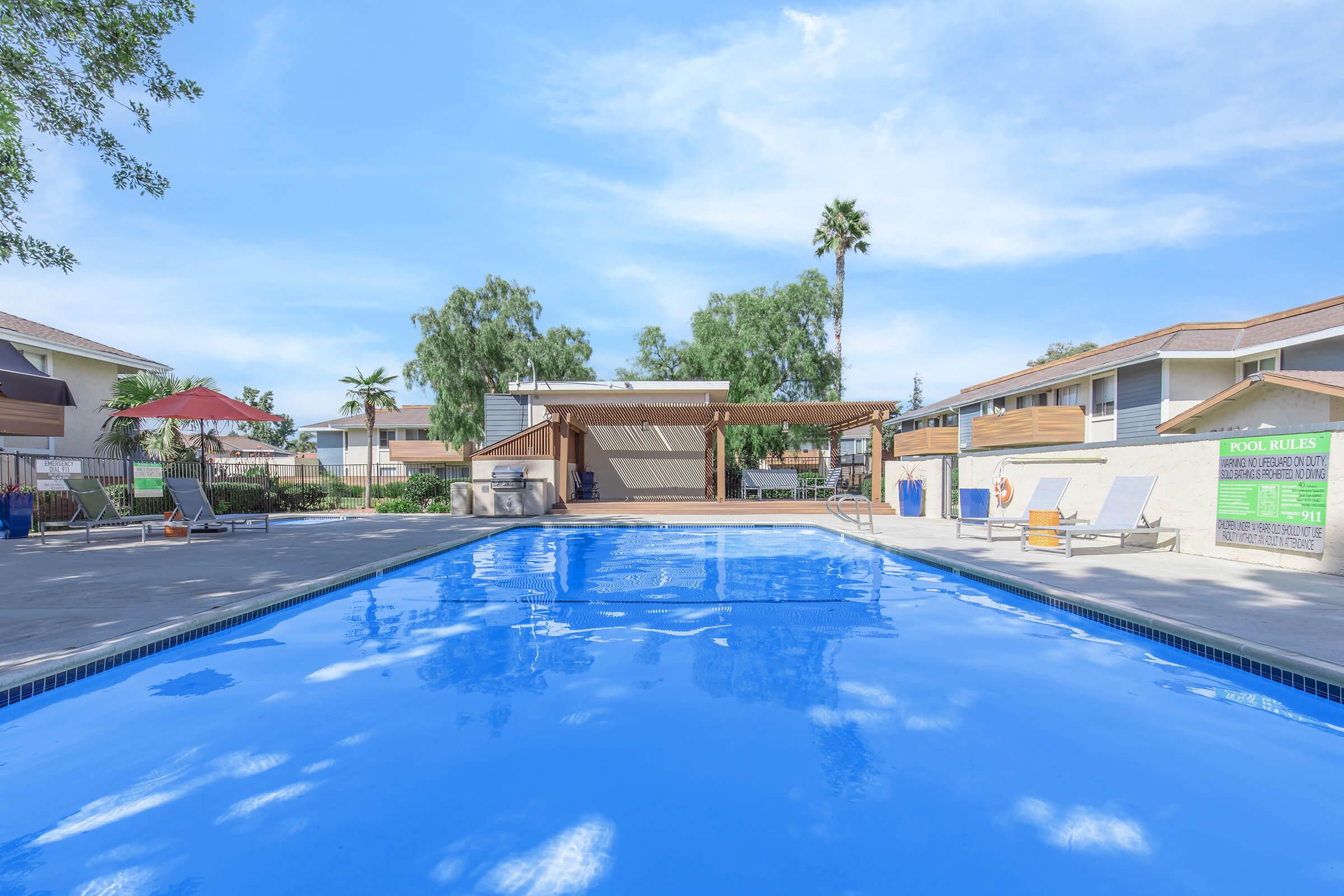 2 Bedroom Apartments in Oceanside CA - The Dylan - Sparkling Swimming Pool with Lounge Seating, and Shaded Area with BBQ Surrounded by Apartments.