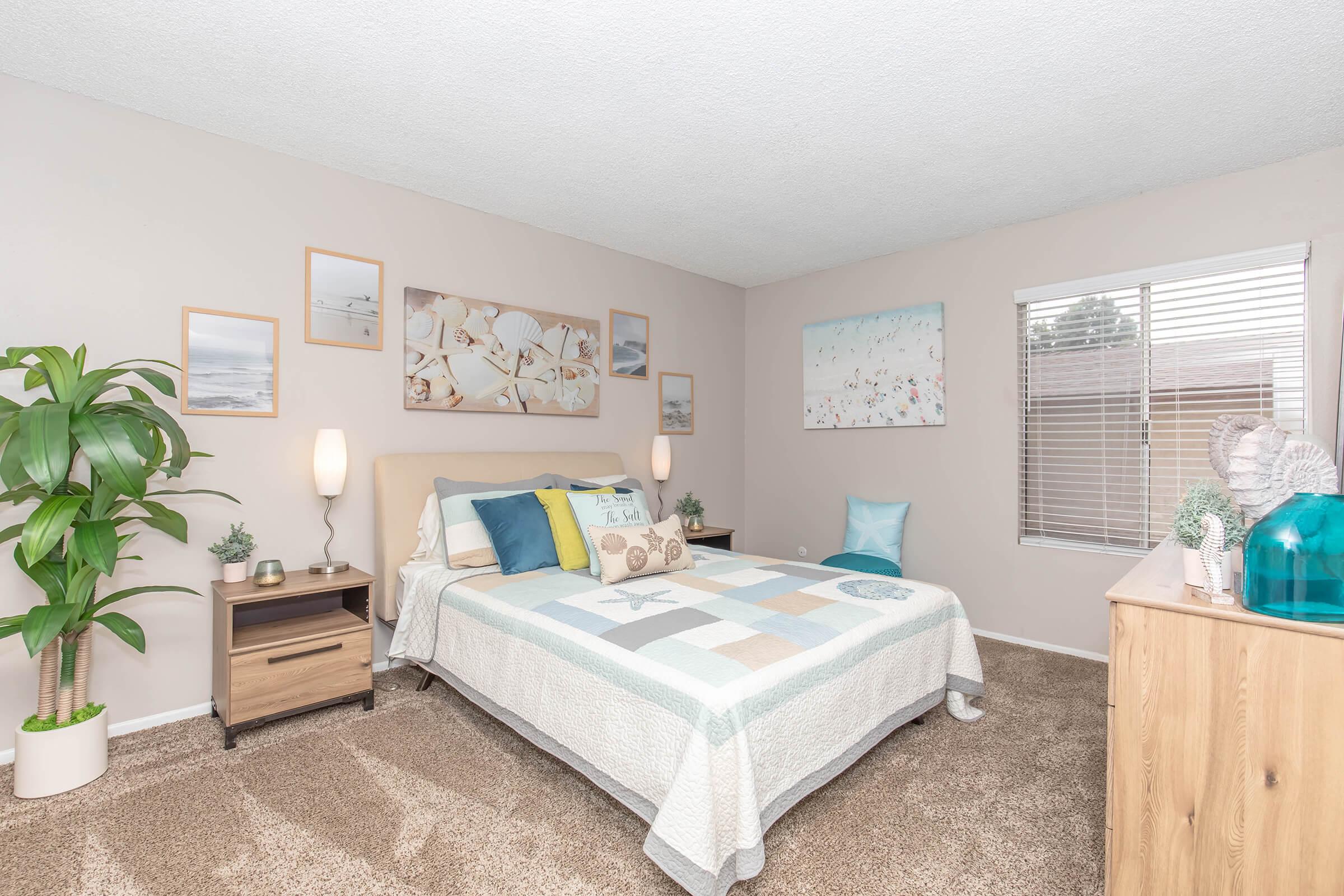 Pet-Friendly Apartments in Oceanside CA - The Dylan - Cozy Bedroom with Plush Carpeting, High Textured Ceilings, and Large Windows with Coverings.