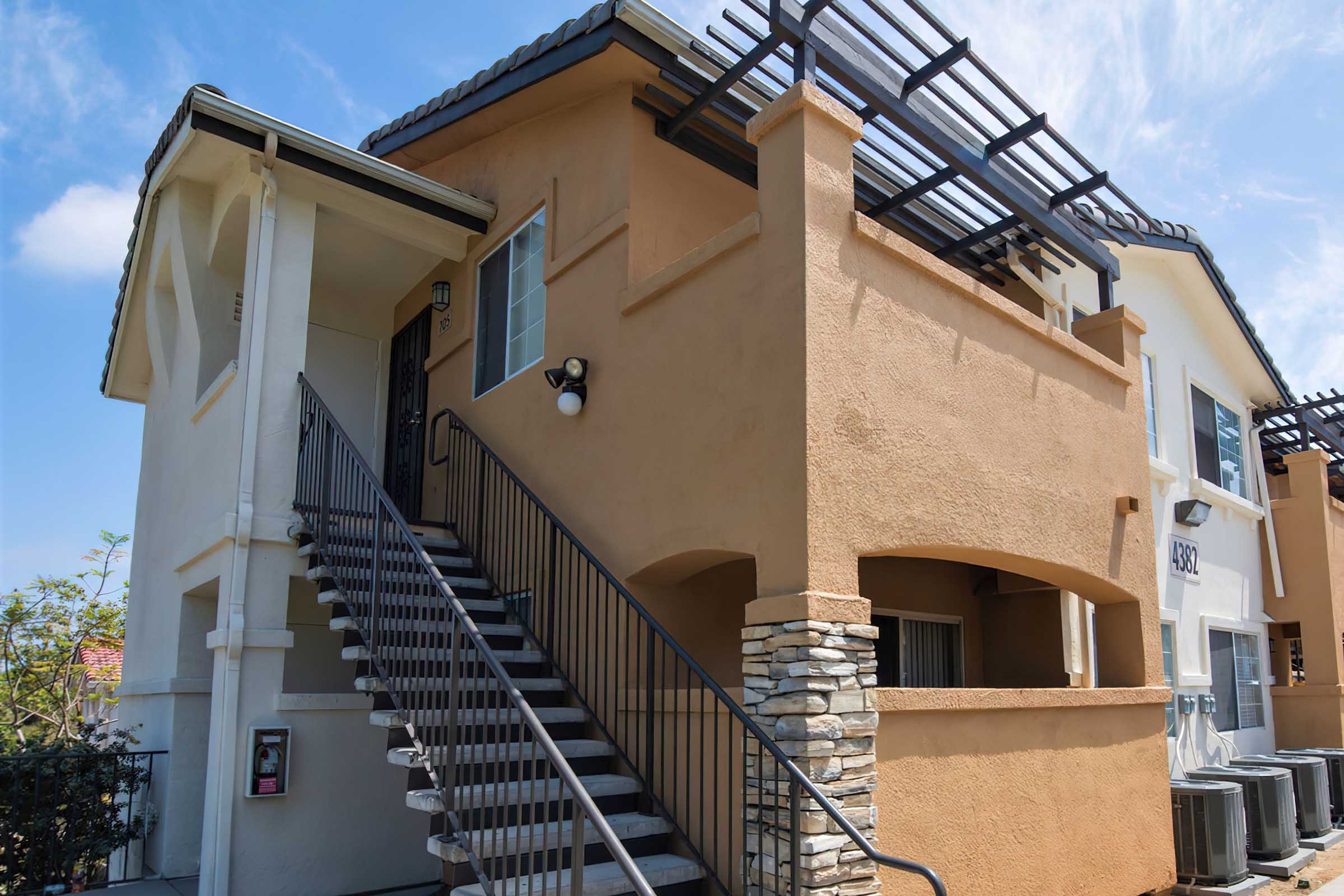 A two-story residential building with a light orange exterior. There is a staircase leading to the upper level, surrounded by railings.