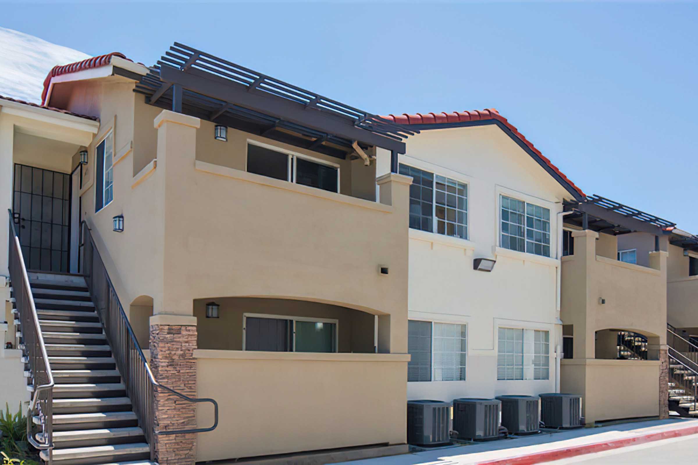 A multi-unit residential building featuring two stories with beige and white exteriors, a red-tiled roof, and shaded balconies.