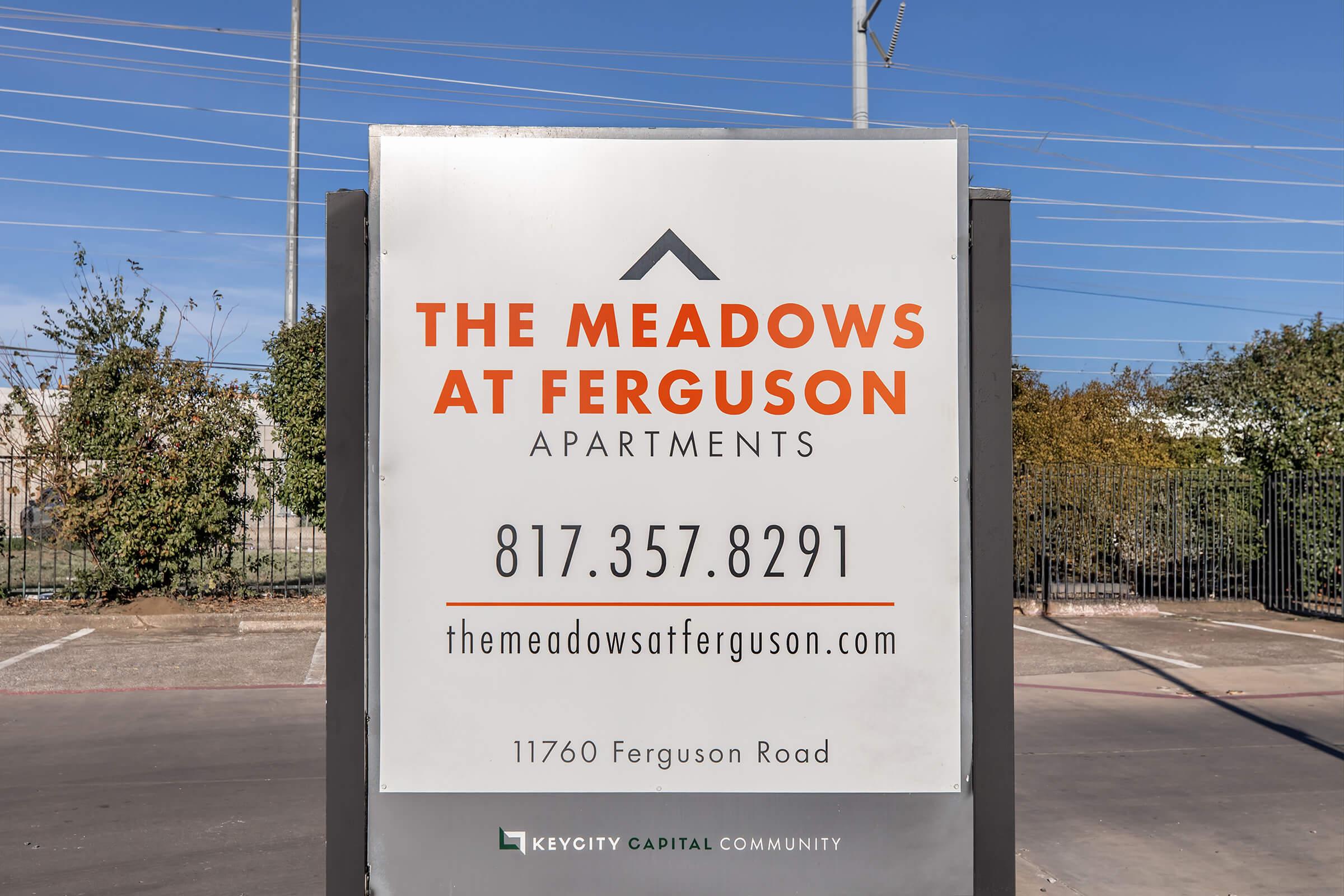 Sign for The Meadows at Ferguson Apartments, displaying the phone number 817-357-8291 and the website themeadowsatferguson.com. Located at 11760 Ferguson Road, the sign is part of a KeyCity Capital Community. Background features trees and power lines.