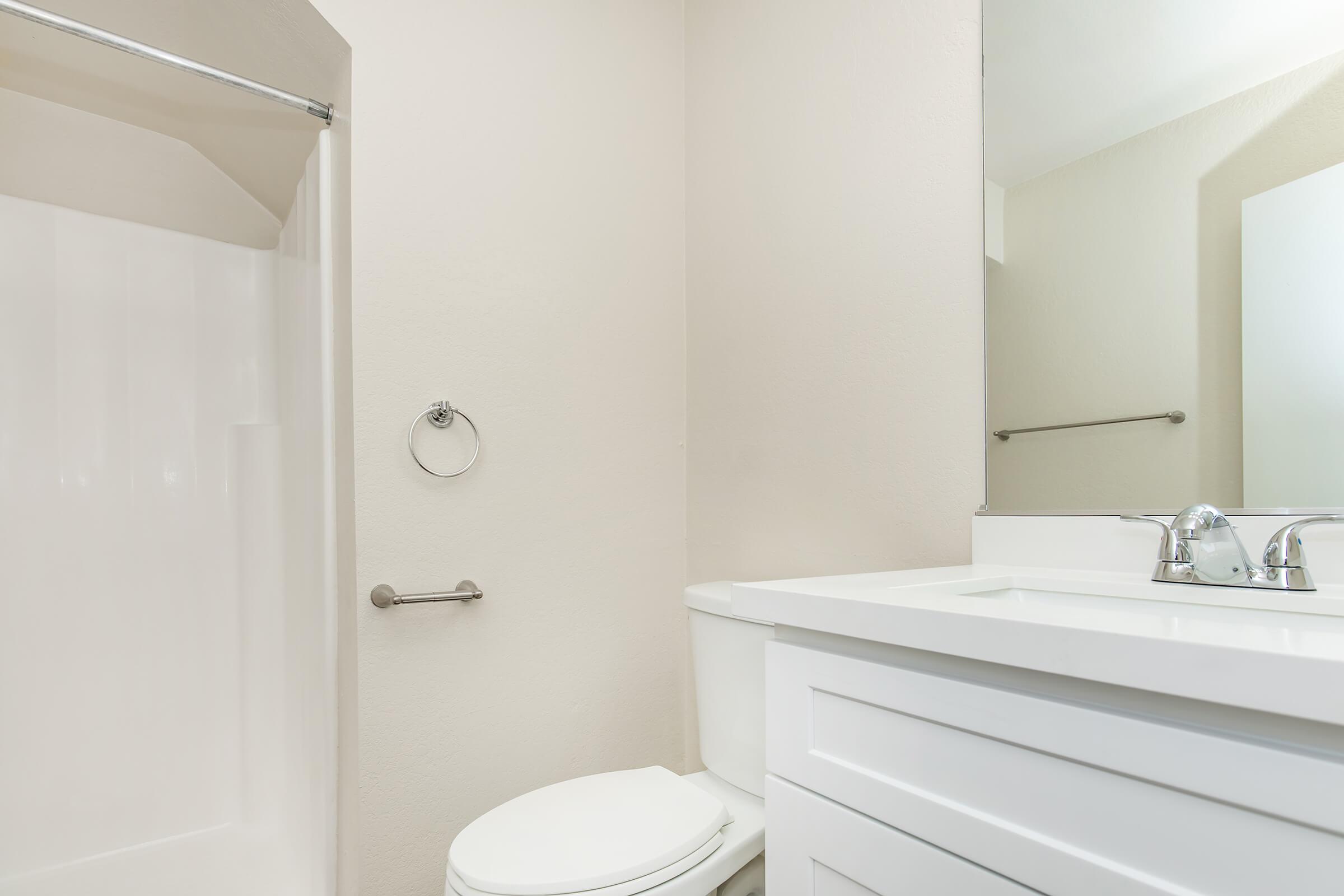 A modern bathroom featuring a white toilet, a sleek countertop with a sink, a mirror above the sink, and a shower space with a glass door. The walls are a soft beige color, creating a clean and inviting atmosphere.